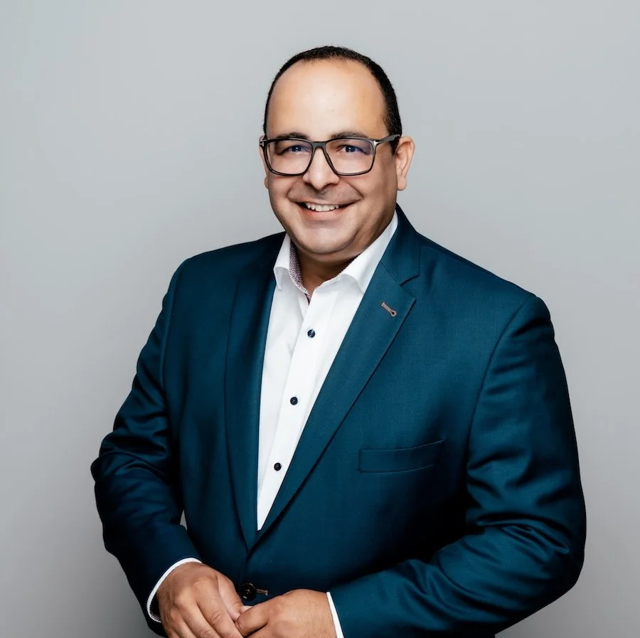 Portrait des lächelnden Mediators Sam Amid vor hellgrauen Hintergrund