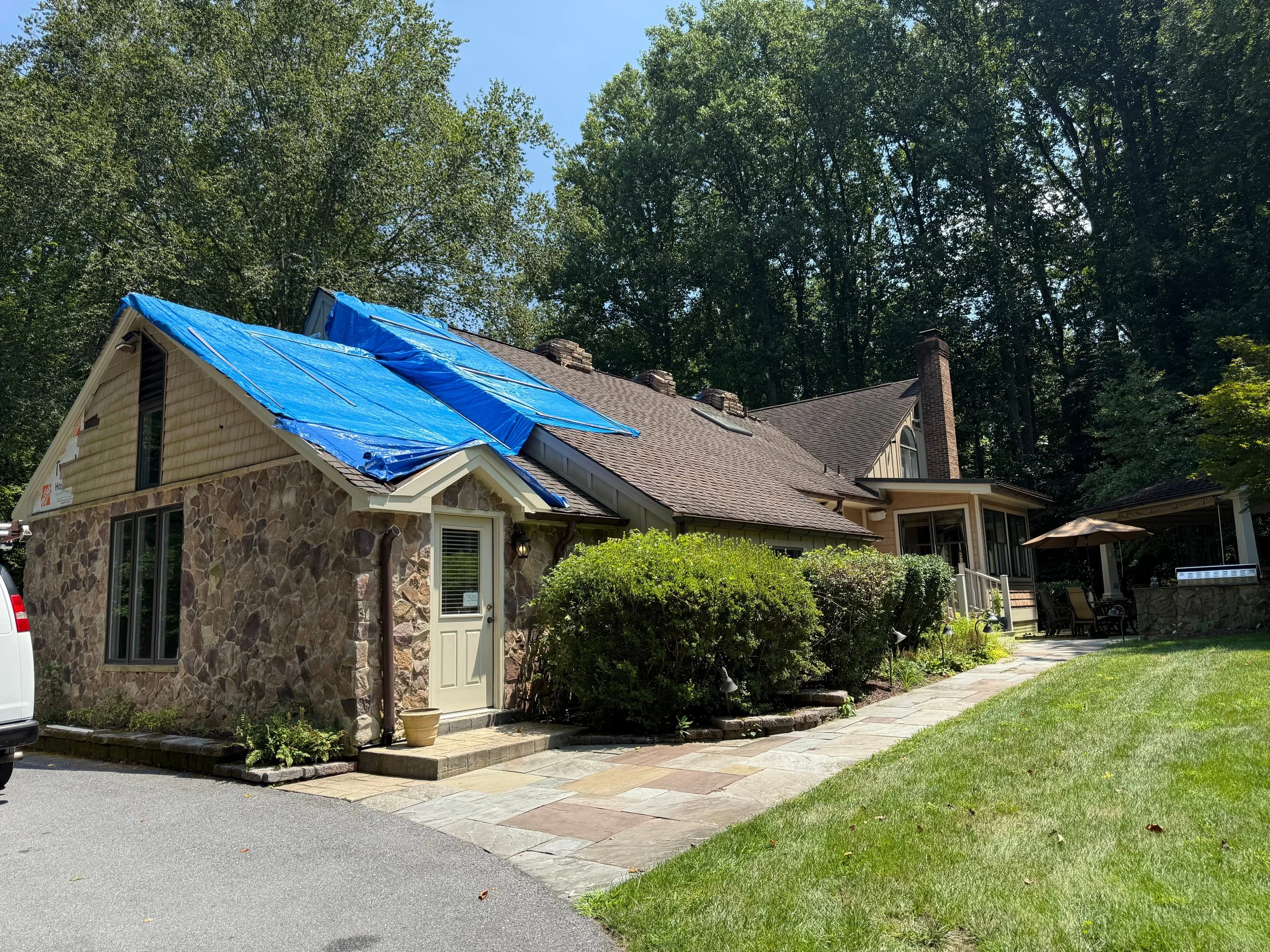 Blue emergency tarp covering a damaged section of a stone-front house roof
