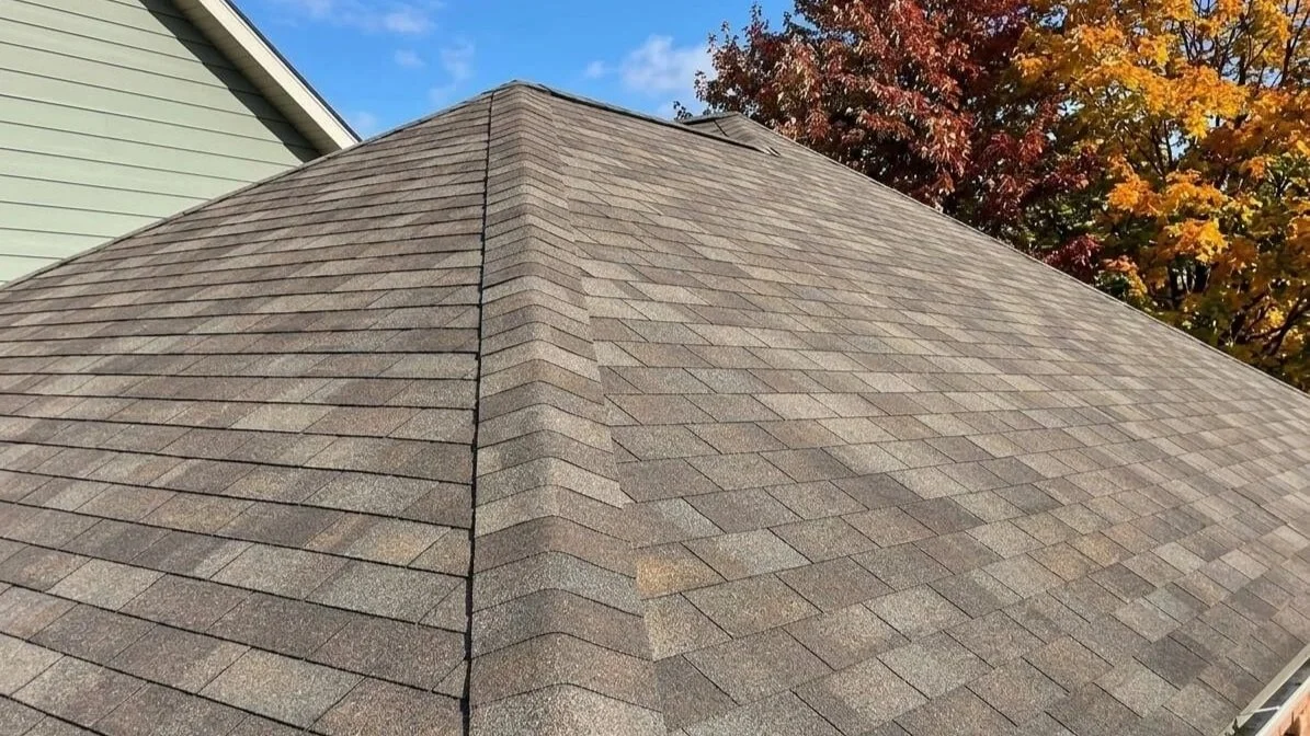 Close-up of a pyramid hip roof with tan architectural shingles on a Maryland home, framed by fall foliage.