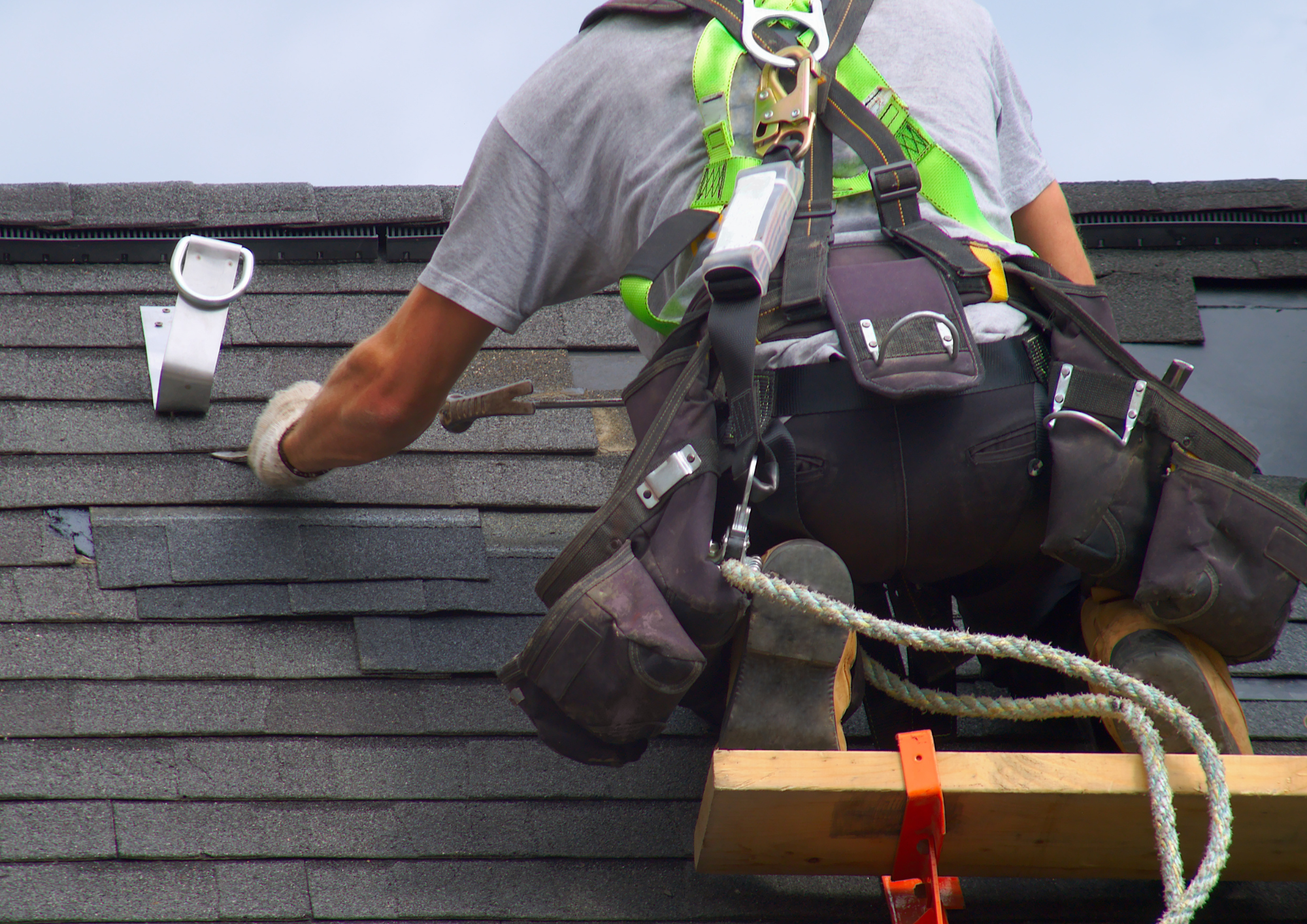 Roofing contractor in safety gear removing shingles
