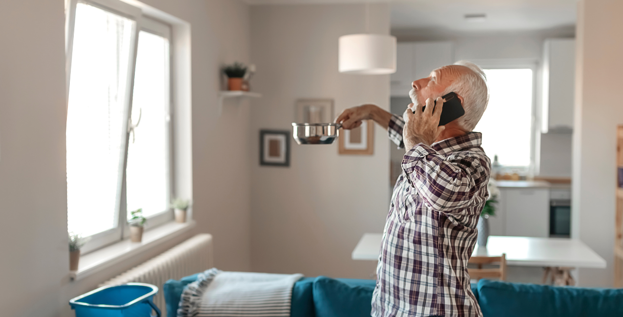 Homeowner holding a pan to catch water dripping from a roof leak