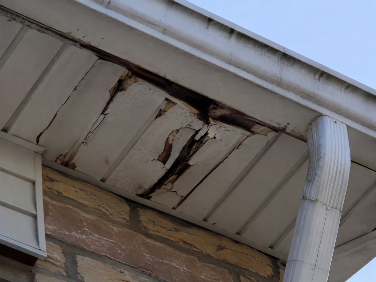 Cracked and deteriorated soffit panels showing signs of moisture damage beneath a home’s roofline.
