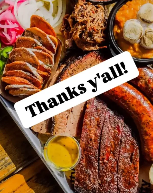 A hearty barbecue meal including sliced brisket, smoked sausage, pulled pork, fried chicken, baked beans with bread rolls, and sliced onions, with a "Thanks y'all!!" message overlaying the image.