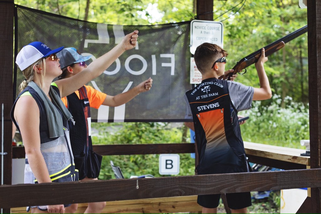 Youth participating in a clay pigeon shooting event, with one holding a shotgun and others observing.