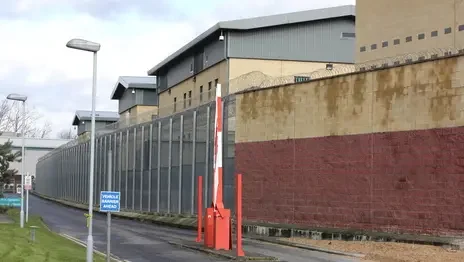 Photograph of large modern building surrounded by a tall, barbed-wire topped fence.