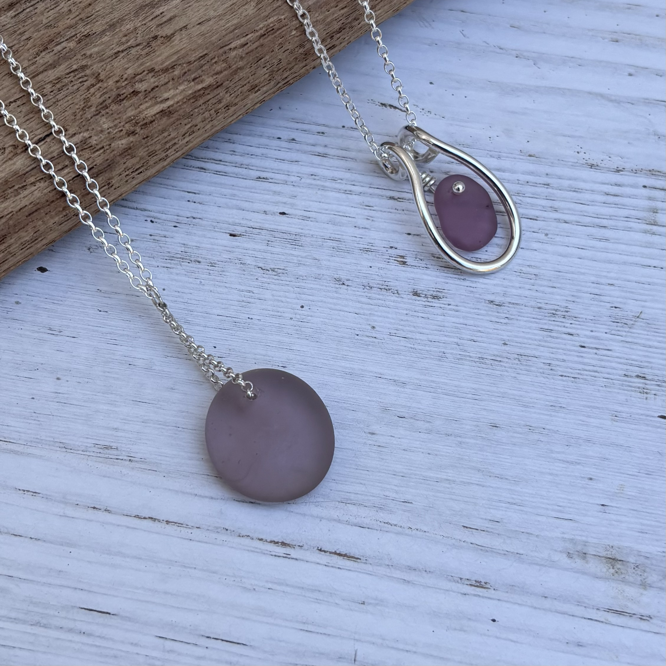 A silver necklace with a large circular pendant resting on a distressed wooden surface