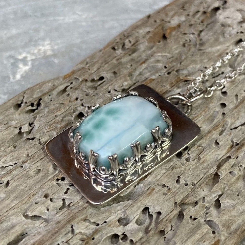 A necklace with a large, oval turquoise gemstone set in an ornate silver setting, placed on a weathered wooden surface.