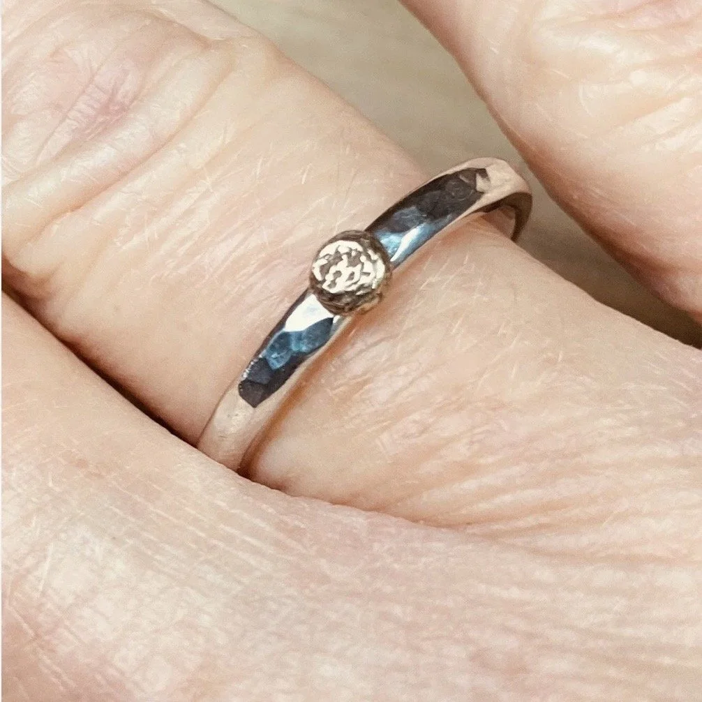 Close-up of a hand wearing a silver ring with a round, textured detail on top.