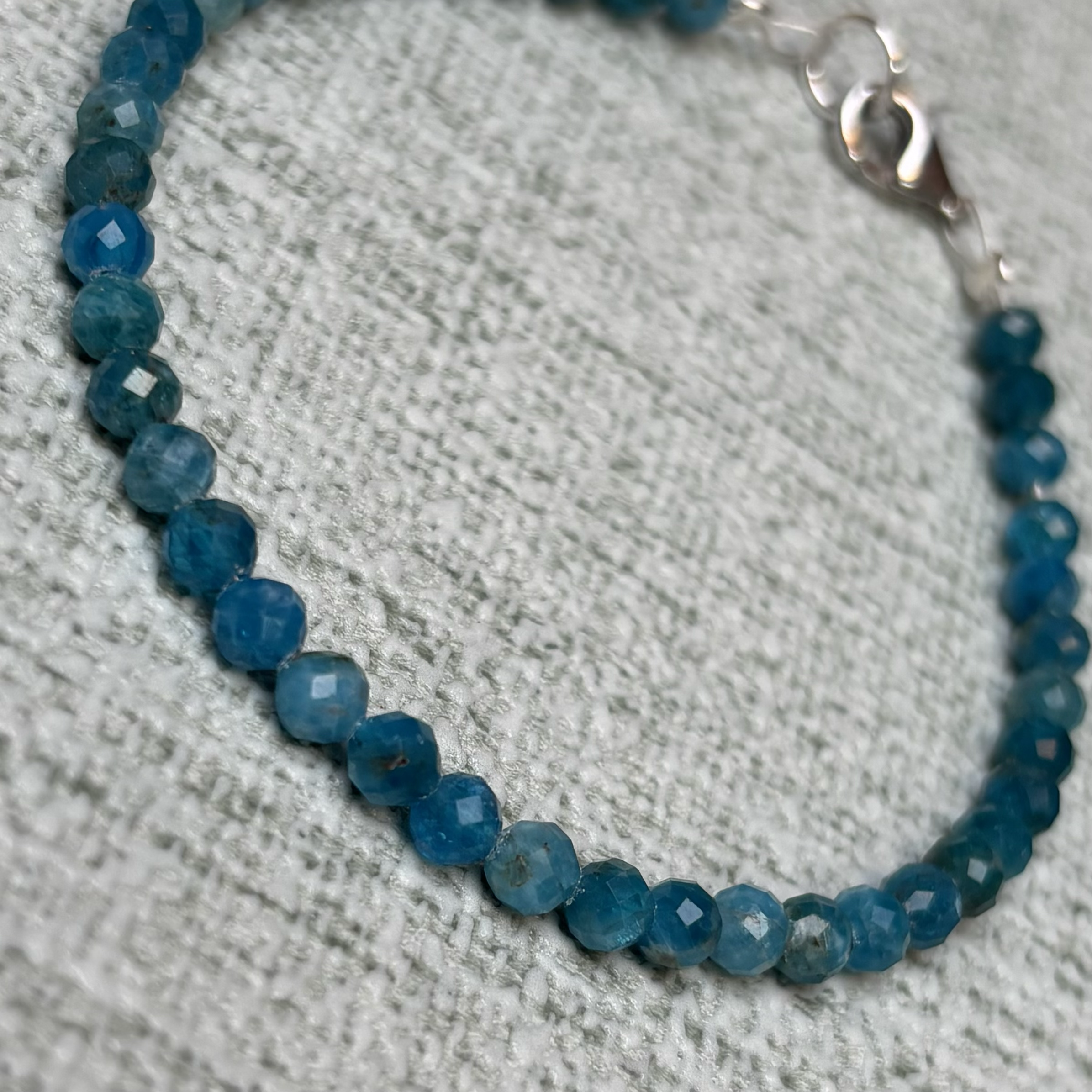 Close-up of a Blue Apatite faceted beaded bracelet arranged in a semi-circle on a textured white background.