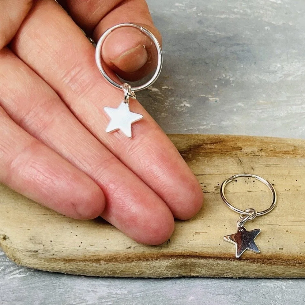 Silver hoop earrings with star-shaped charms, one placed on fingers and another on wooden surface.