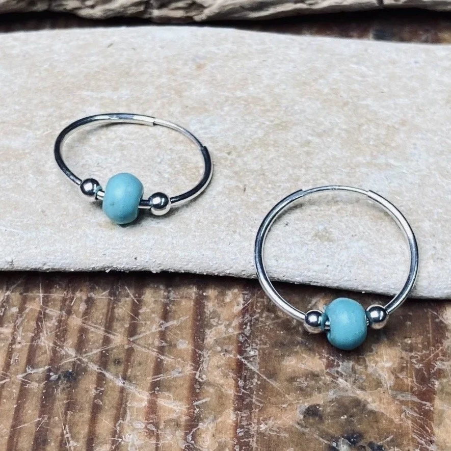 Pair of earrings with blue beads and silver rings placed on a wooden surface.