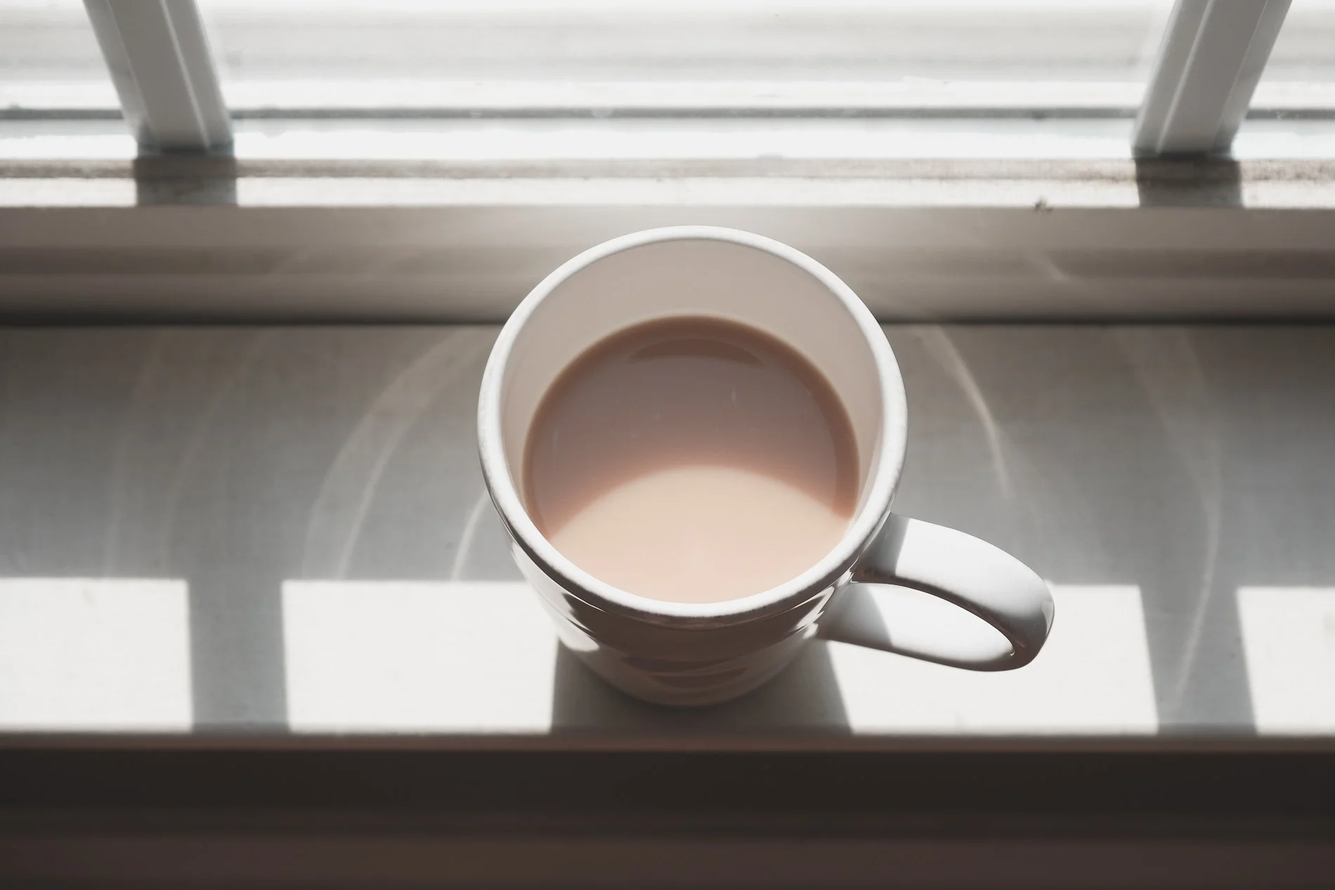 white mug of creamy tea on white windowsill