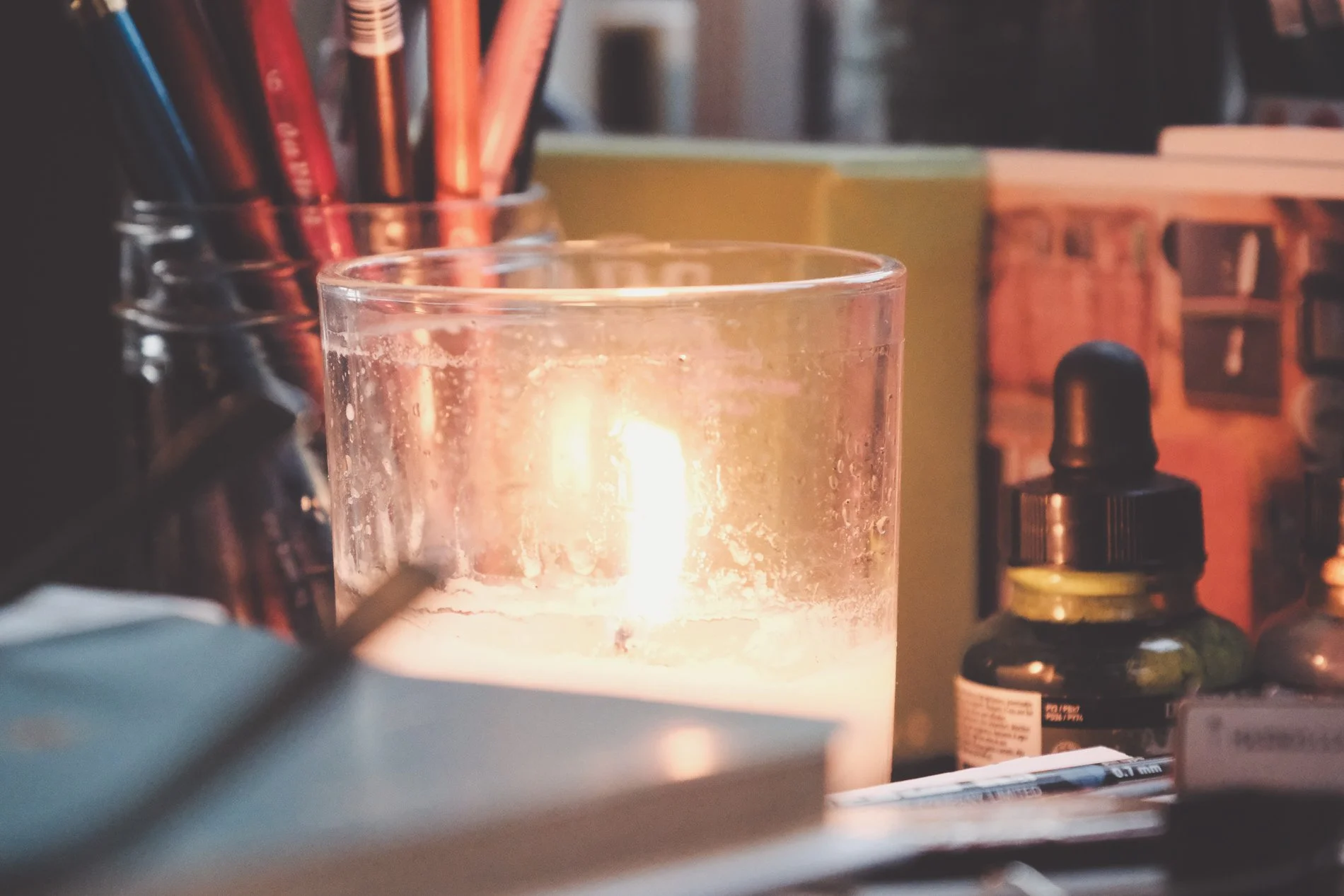 lit candle on deck with jar of pencils and bottle of green ink