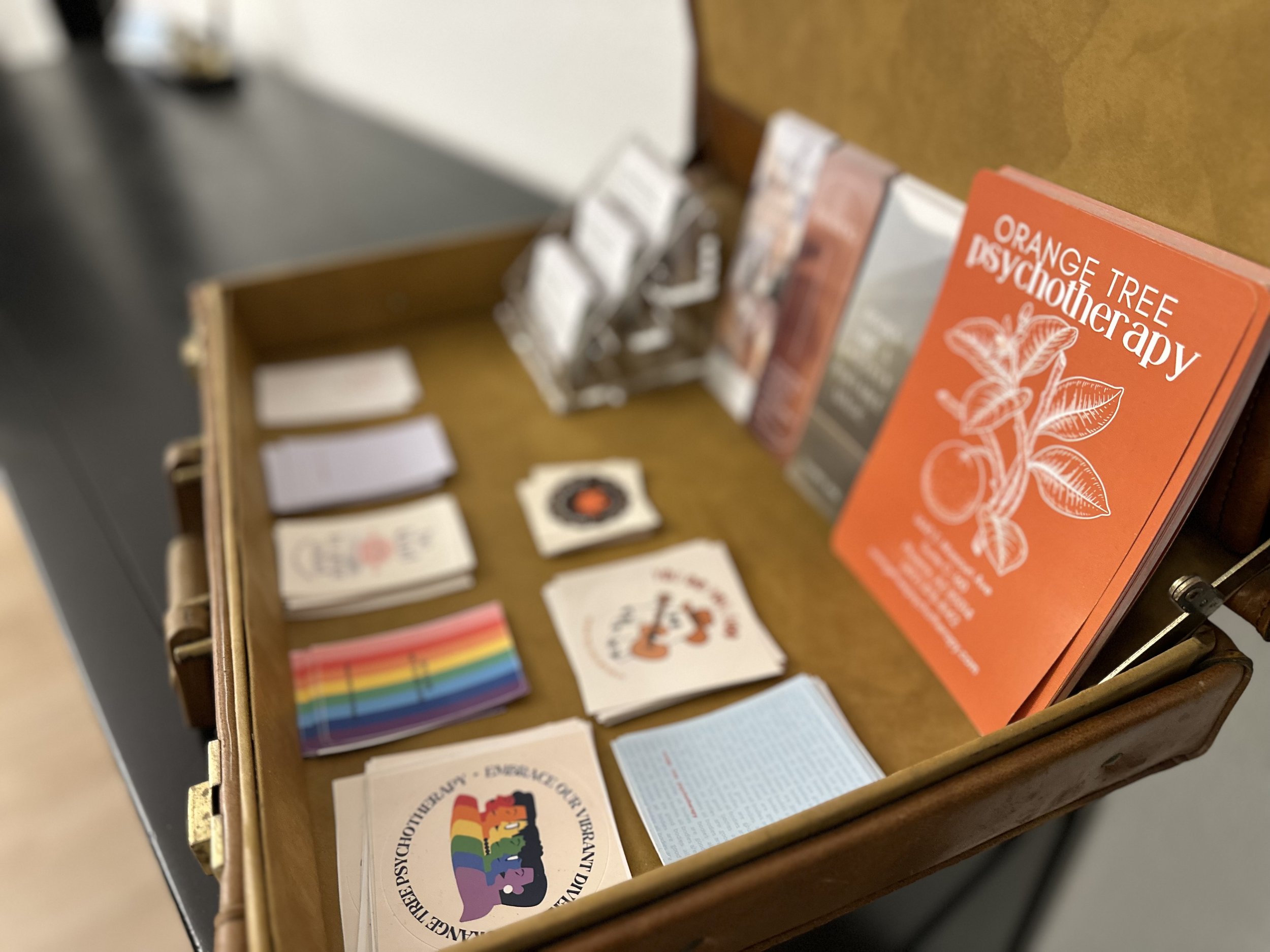 Open suitcase displaying psychotherapy pamphlets, cards, and a flyer titled "Orange Tree Psychotherapy"
