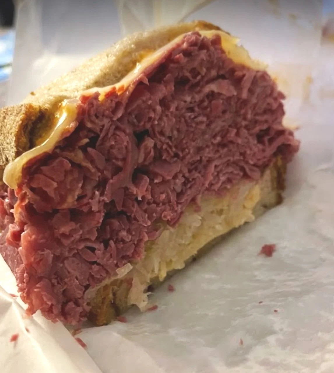 A close-up of a corned beef sandwich with shredded beef, mustard, and a bulkie roll on a piece of parchment paper.