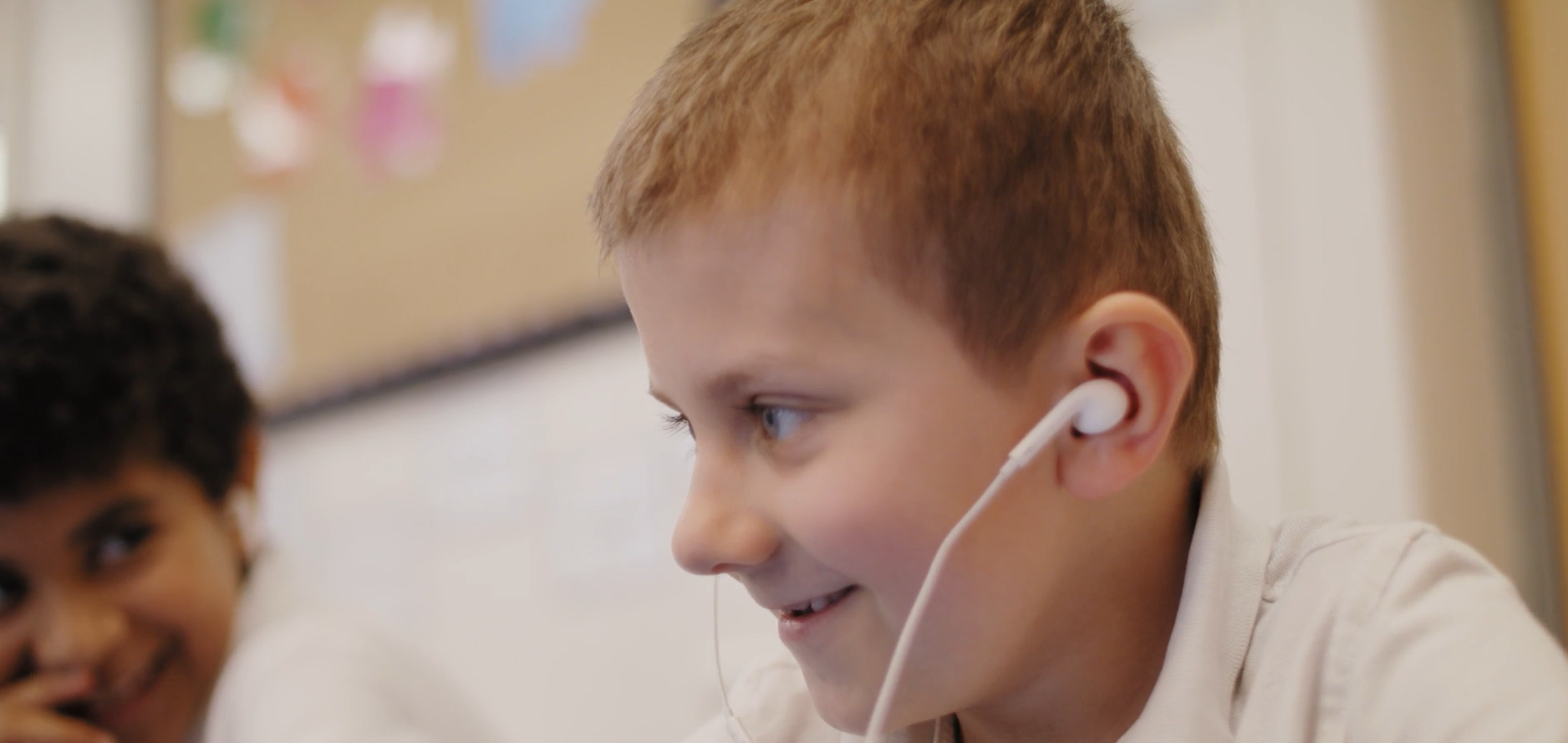 A young child using white, wired earphones. A snapshot taken from a Dell, Microsoft and L.E.A.D. IT Services promotional video taken at Hogarth Academy.