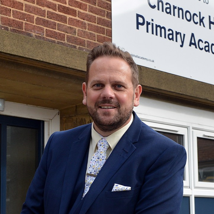 Headshot image of Paul Burgess infront of a building with a sign that says "Charnock Hall Primary Academy"