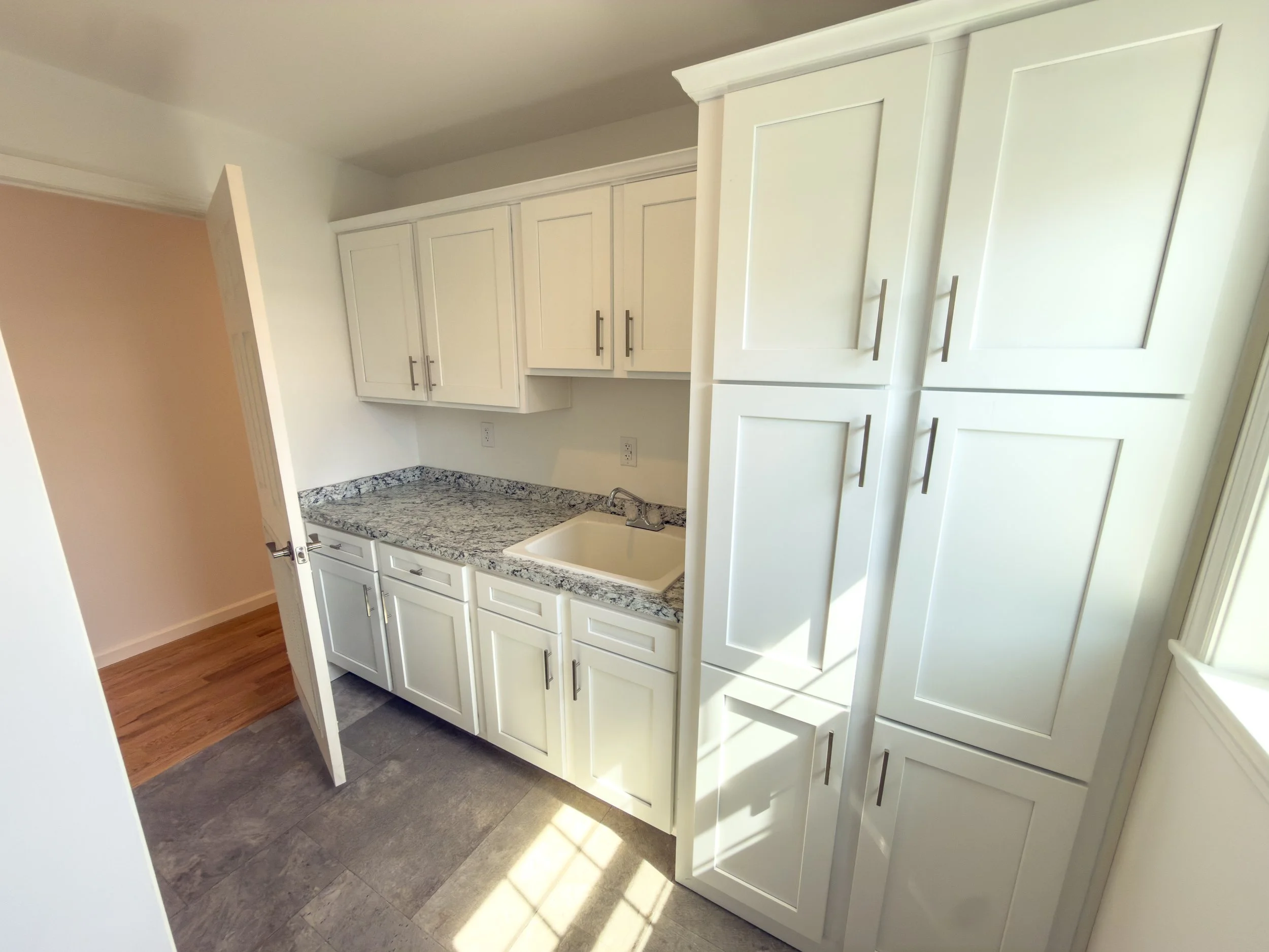 Laundry room with white cabinets, countertop space, sink, beige wall, and wooden and tile flooring.