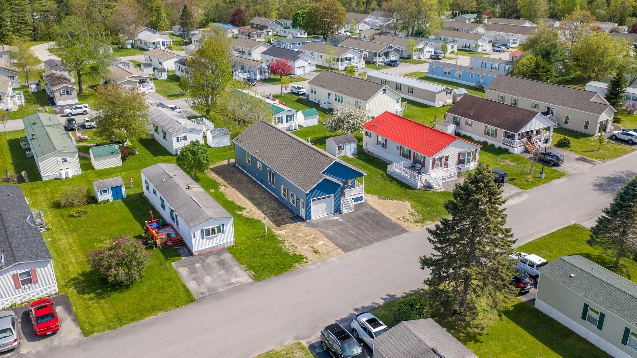 Aerial view of a residential neighborhood, Pinecrest, with single-family houses, green lawns, trees, and parked cars.