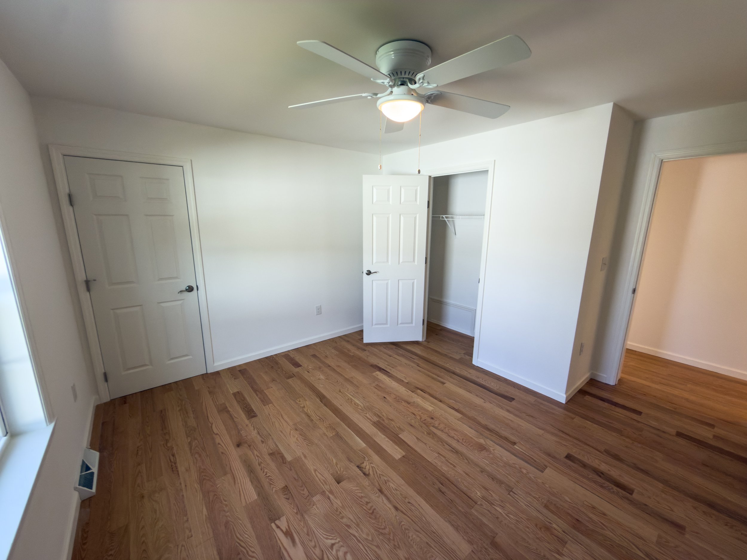Versatile bedroom or bonus room with hardwood floors, white walls, ceiling fan, and an open closet — a flexible space in a Manufactured Home