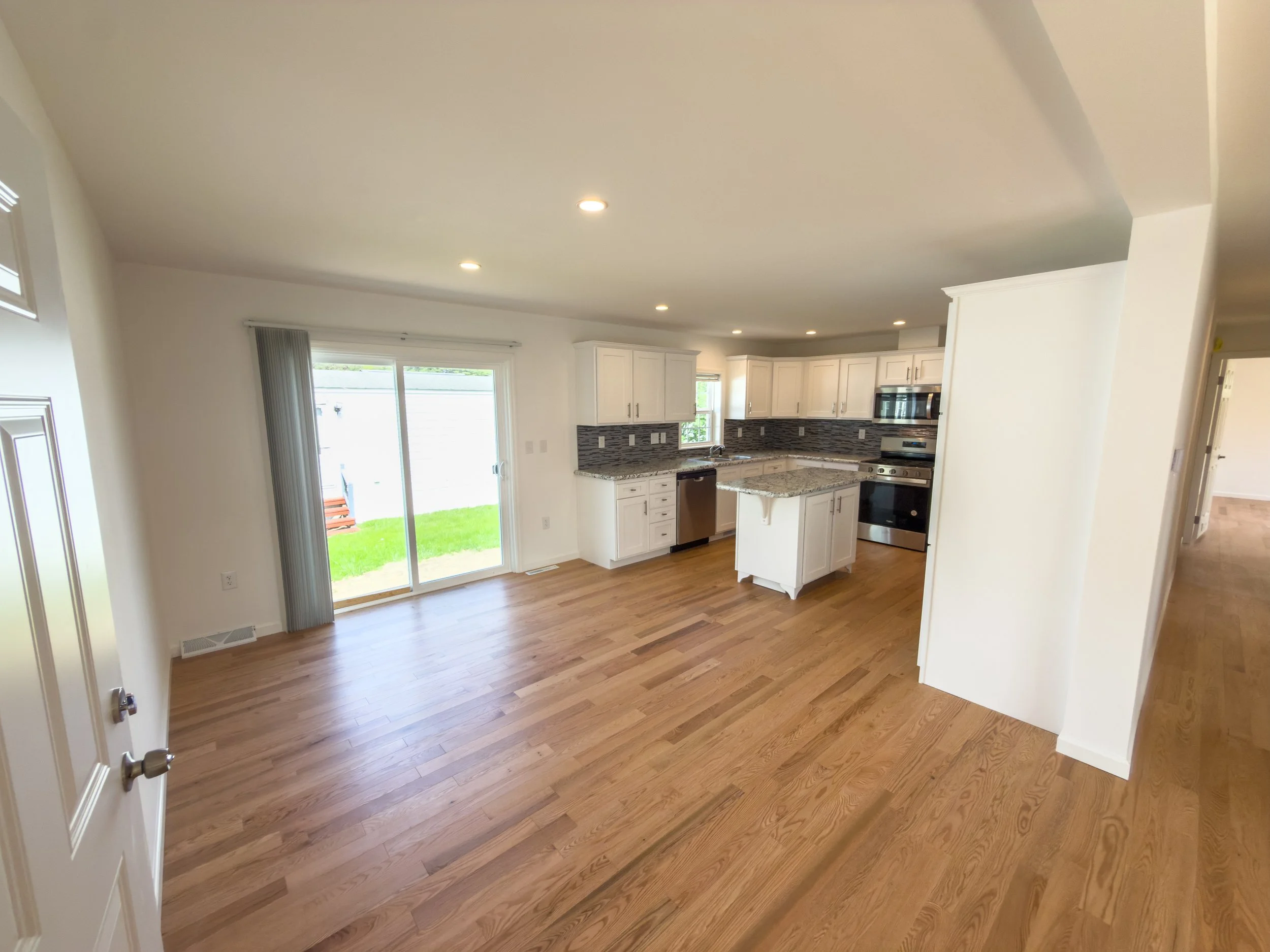 Open-concept kitchen and living room with hardwood floors, white shaker cabinets, countertops, a kitchen island, and sliding glass doors to the backyard — a bright and modern interior in a Manufactured Home