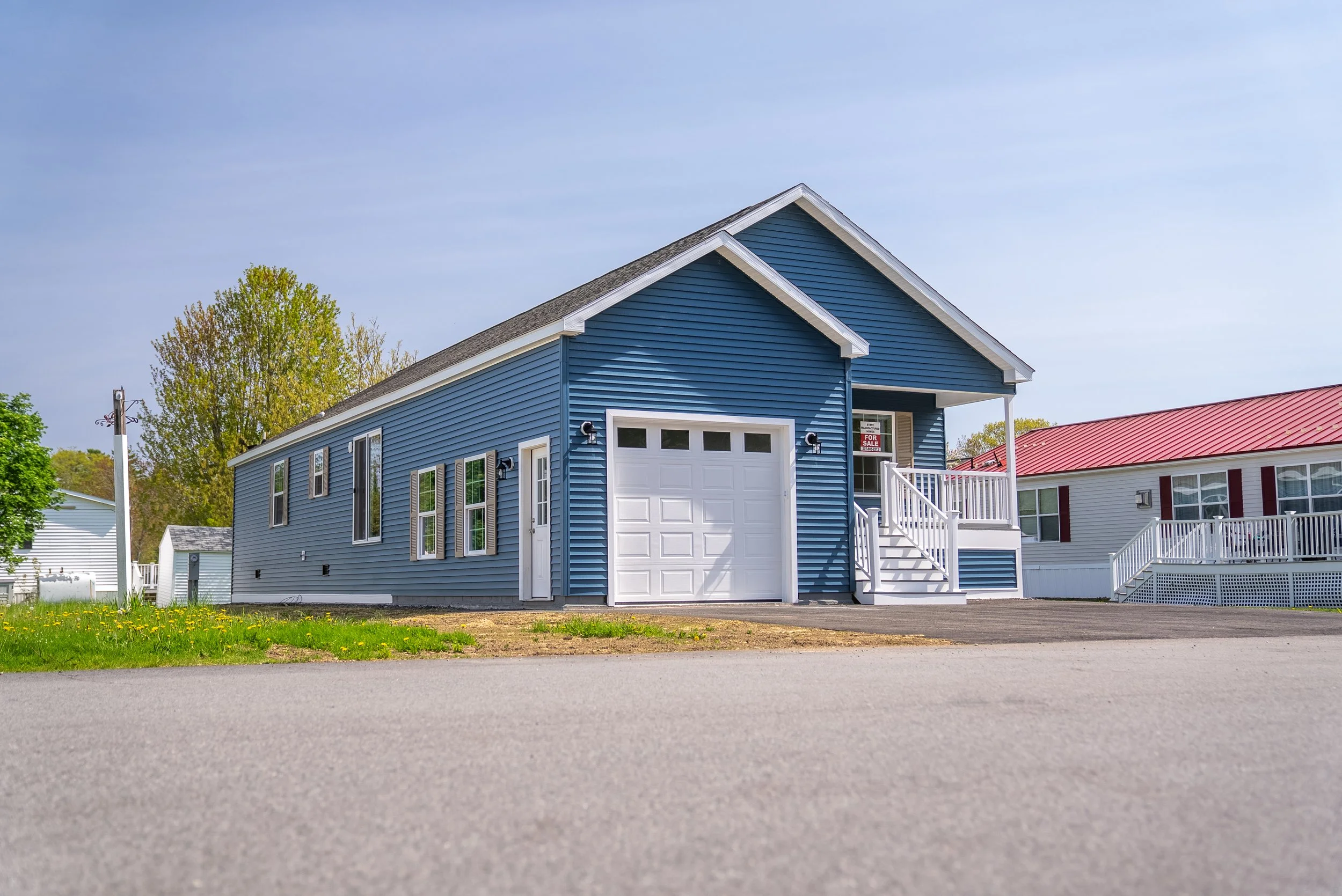 Close-up exterior view of a blue modular manufactured home with a white attached garage door, front porch staircase, and attractive curb appeal in a State Manufactured Homes community