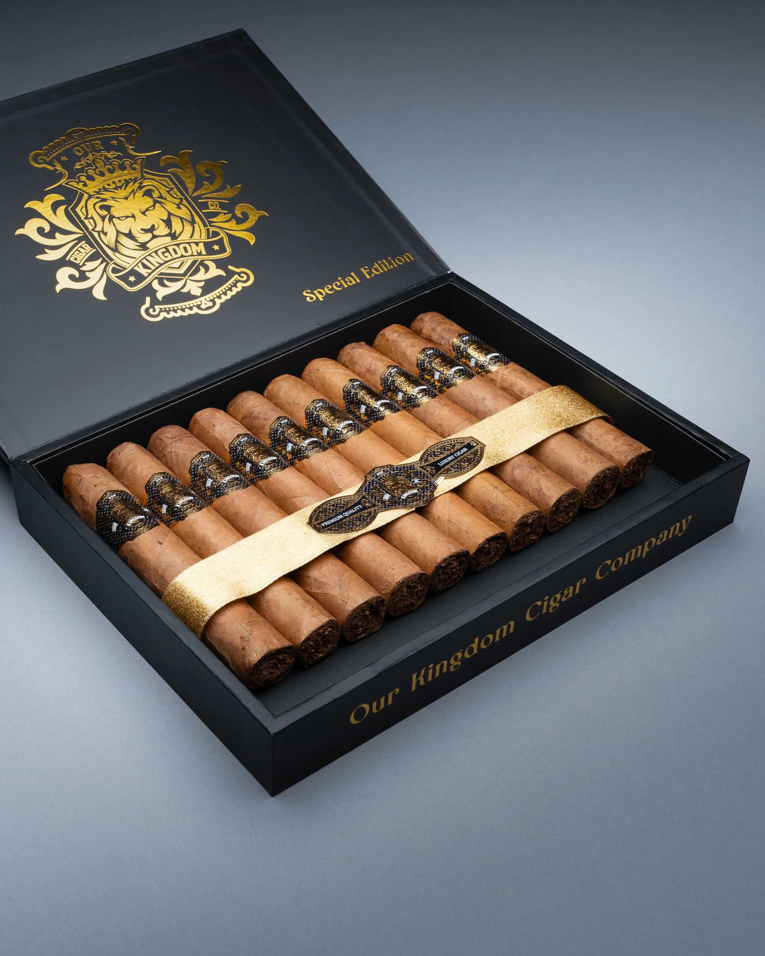 A black box of cigars with gold lettering that reads "Our Kingdom Cigars Company" and "Special Edition." The cigars are neatly arranged in the box with black and gold bands and a gold ribbon across them.