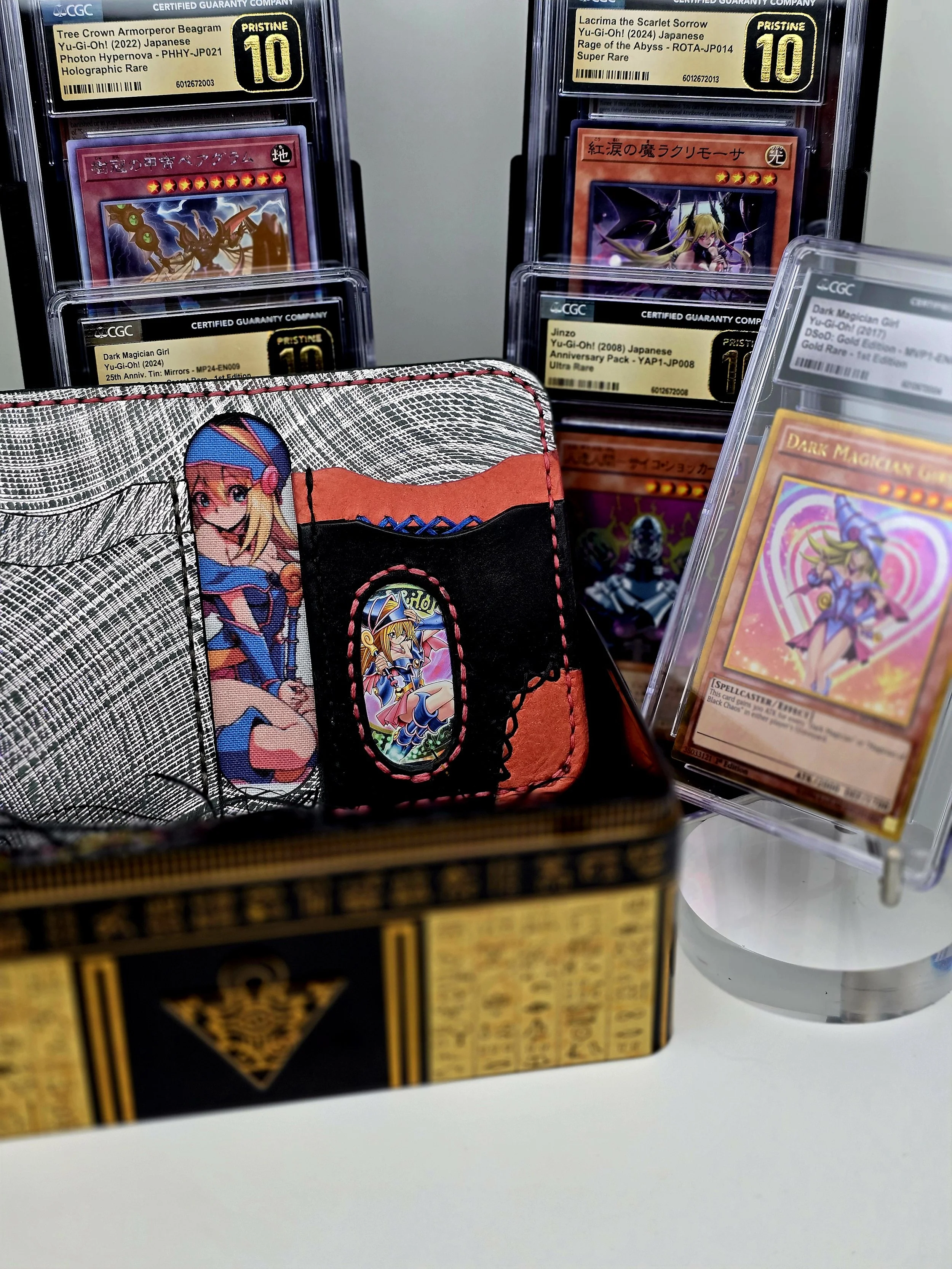 Collection of trading cards, including Yu-Gi-Oh! cards in protective cases and a colorful card holder with anime-style artwork, displayed on a white surface.