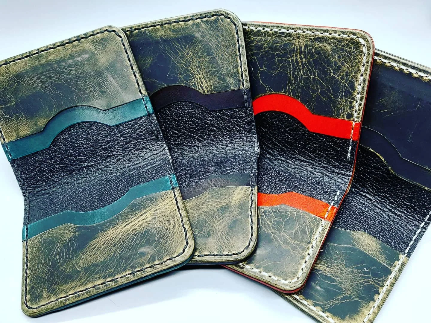 Three leather wallets with different colored stripes on the inside, positioned upright and open to display the interior pockets.