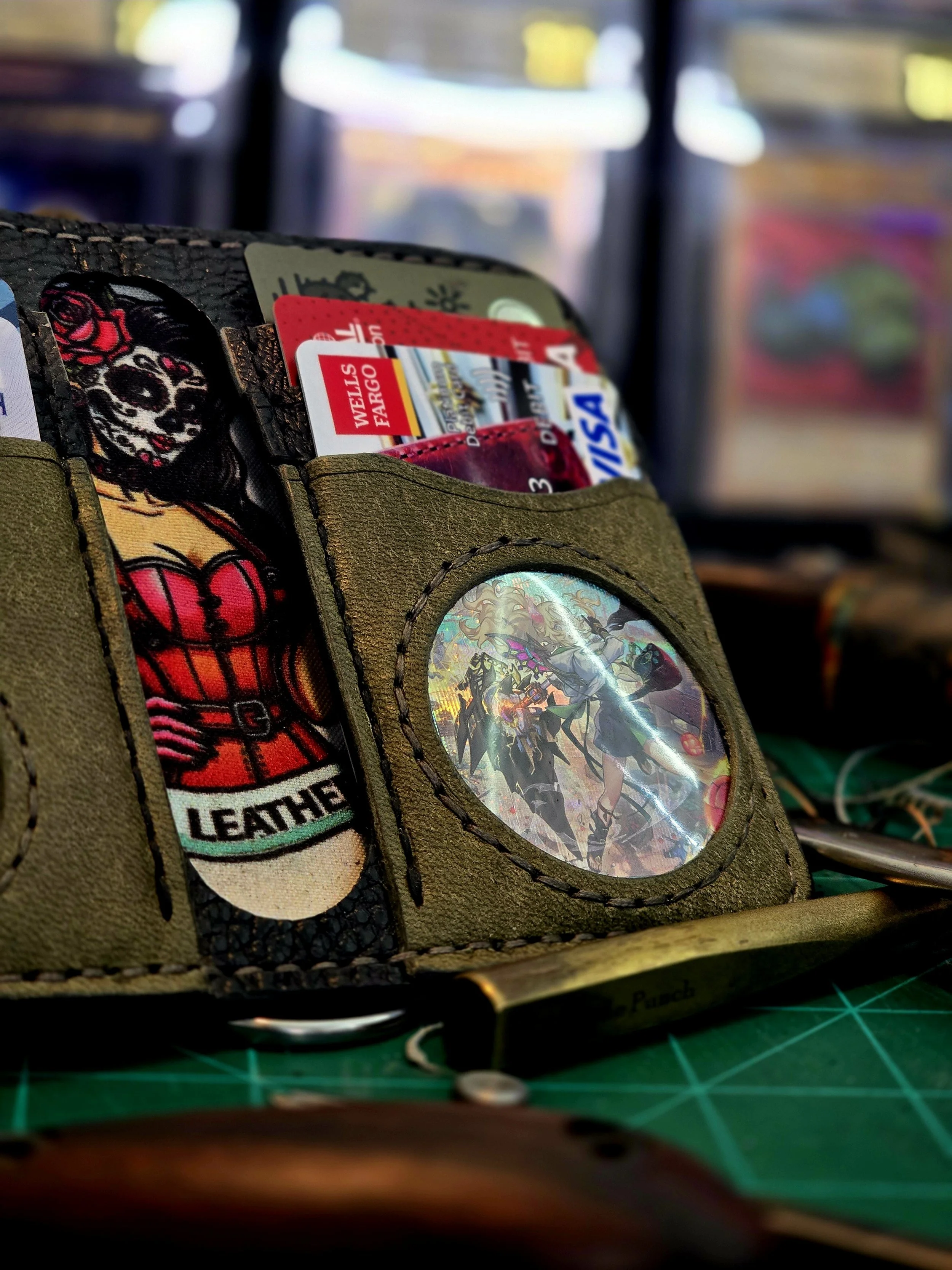 A wallet with colorful patches and a holographic circle, containing credit cards, resting on a green cutting mat with tools nearby.