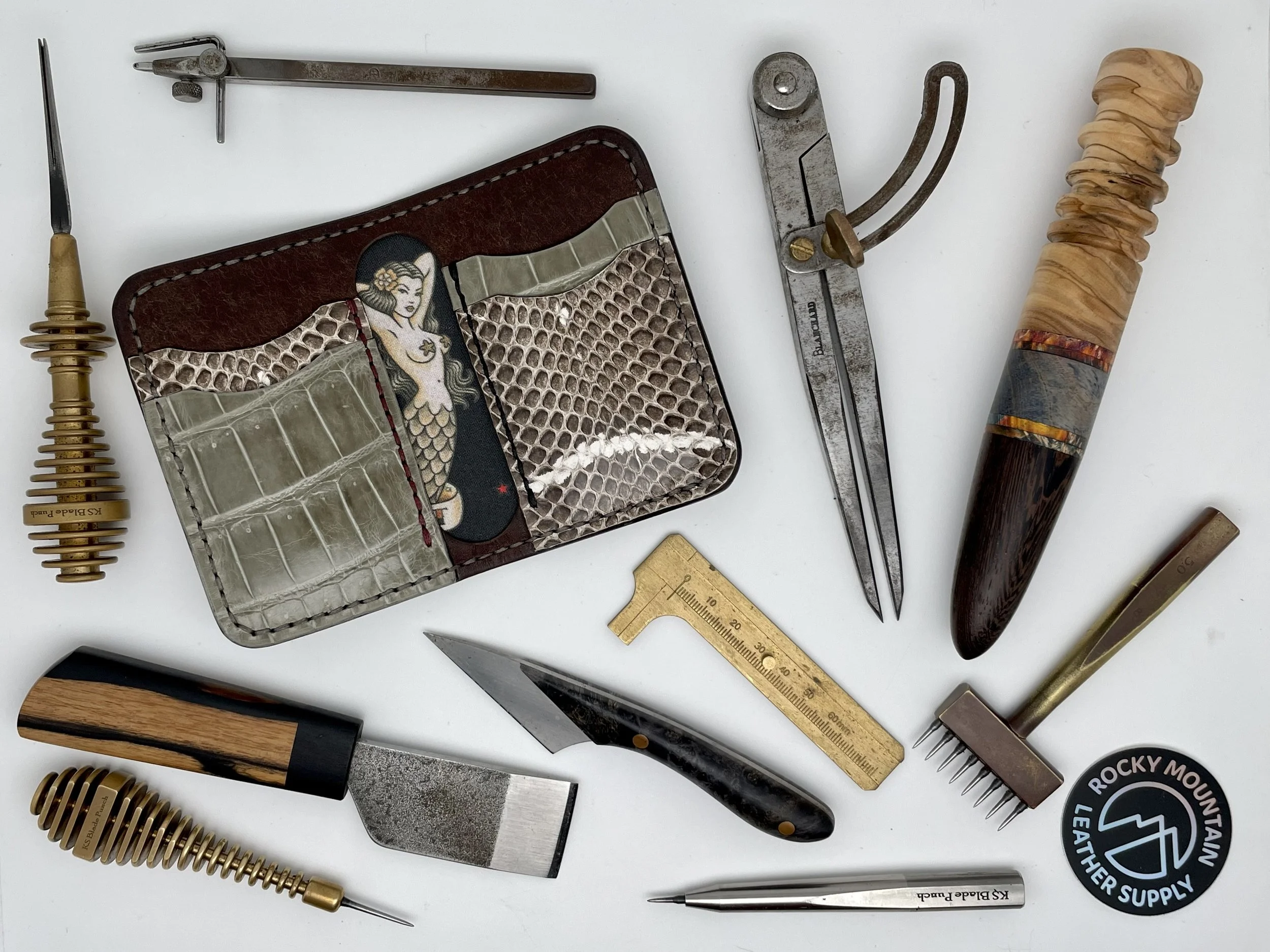 Collection of leatherworking tools and supplies, including knives, prong pushers, a ruler, a branding iron, and a leather craft wallet.