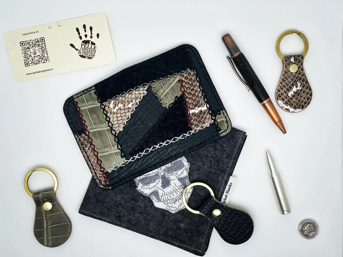 A collection of snake-skin patterned accessories including keychains, a wallet, and a pouch, along with a black and copper pen, an empty coin, and a business card with a handprint design on a white surface.