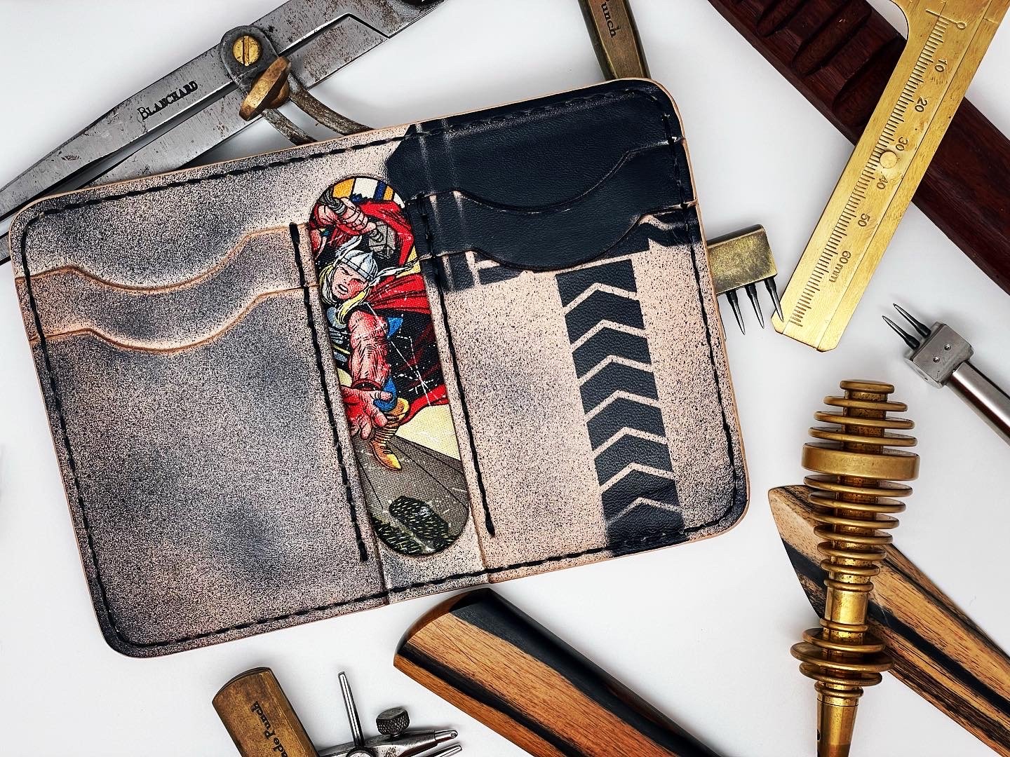 A wallet with a comic book superhero design on the inside, surrounded by various vintage tools and mechanical parts on a white surface.