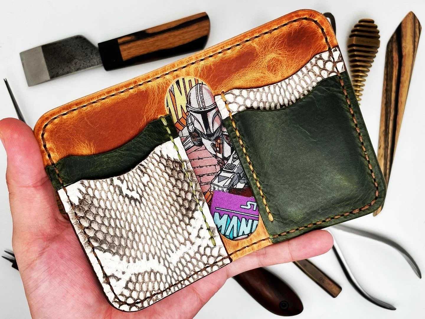 Hand holding a wallet with card slots, featuring a Star Wars Mandalorian character illustration, with various cooking and kitchen tools in the background.