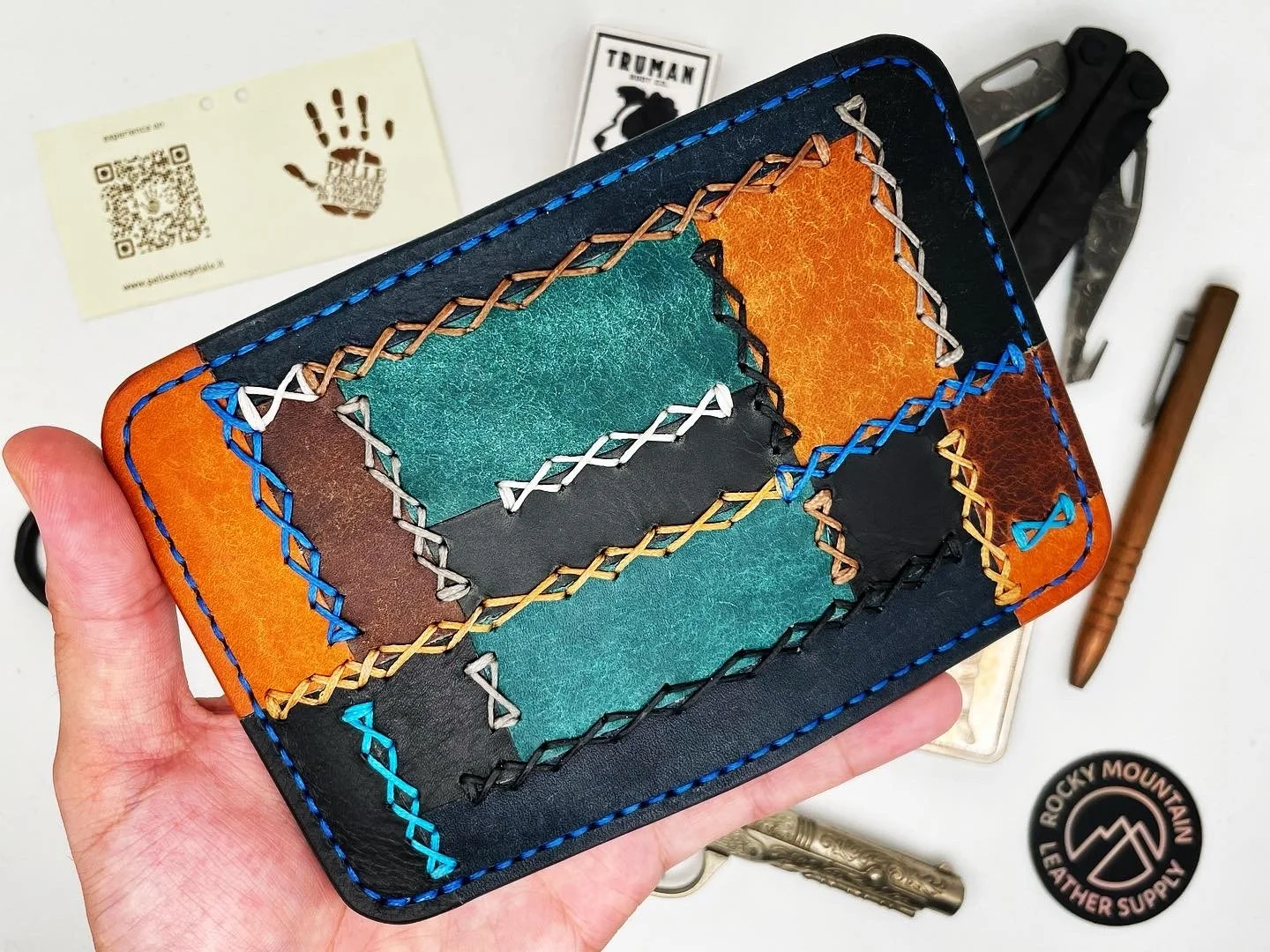 Colorful leather wallet with multicolored stitched patches, held in hand, surrounded by keychain, pen, and a Rocky Mountain leather sticker.