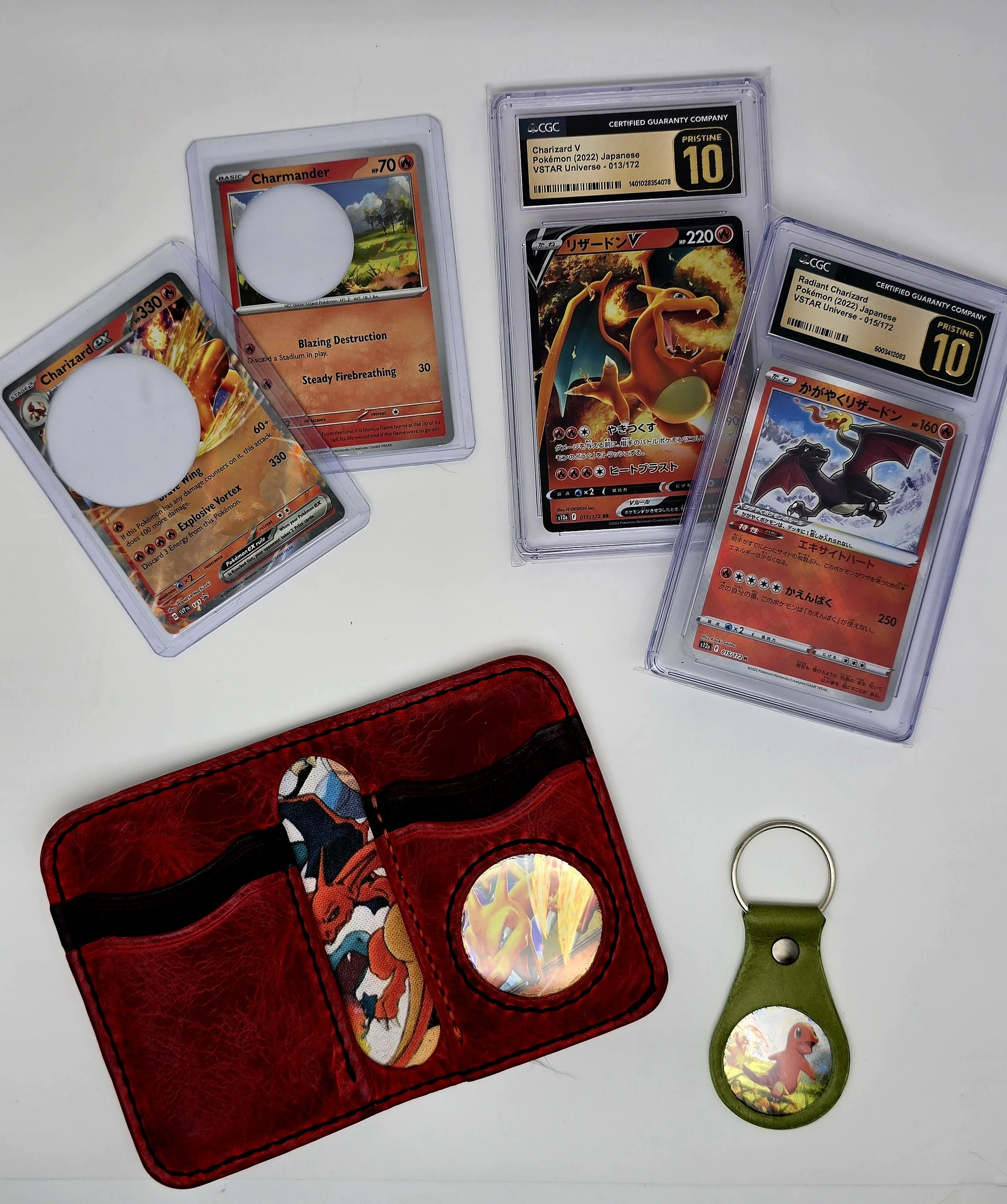 Three Pokémon cards in protective cases, a red Pokémon cardholder with Pokémon stickers, a Pokémon keychain, and a Pokémon trading card pegboard all related to Charizard.