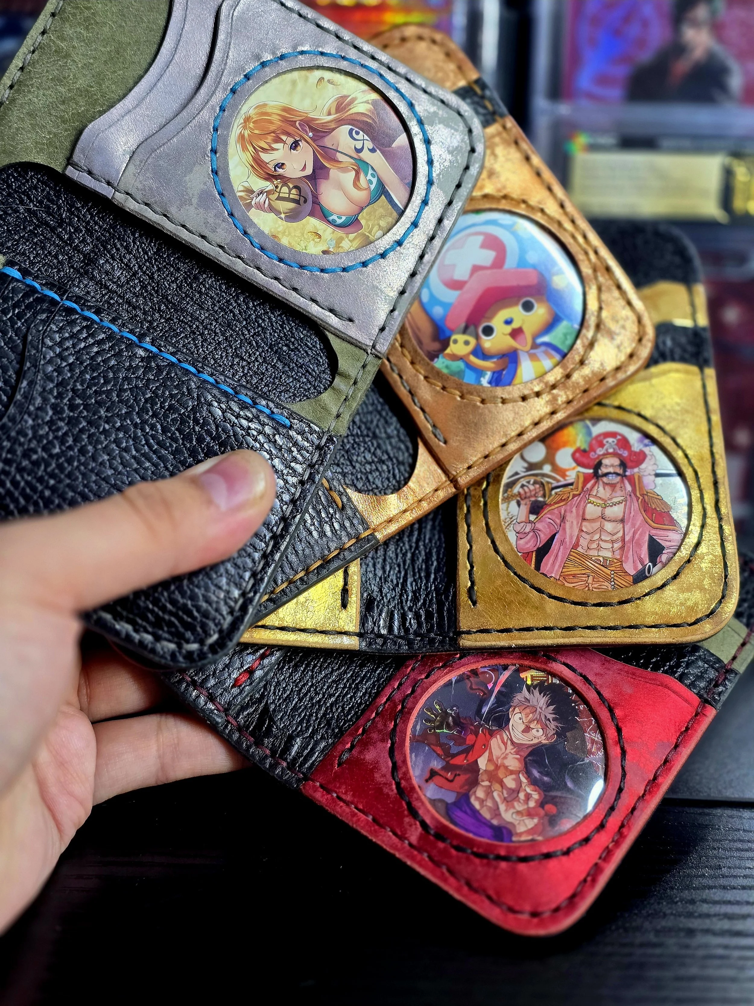 Collection of colorful, anime-themed leather wallet pouches with circular character images on the front, being held in hand.