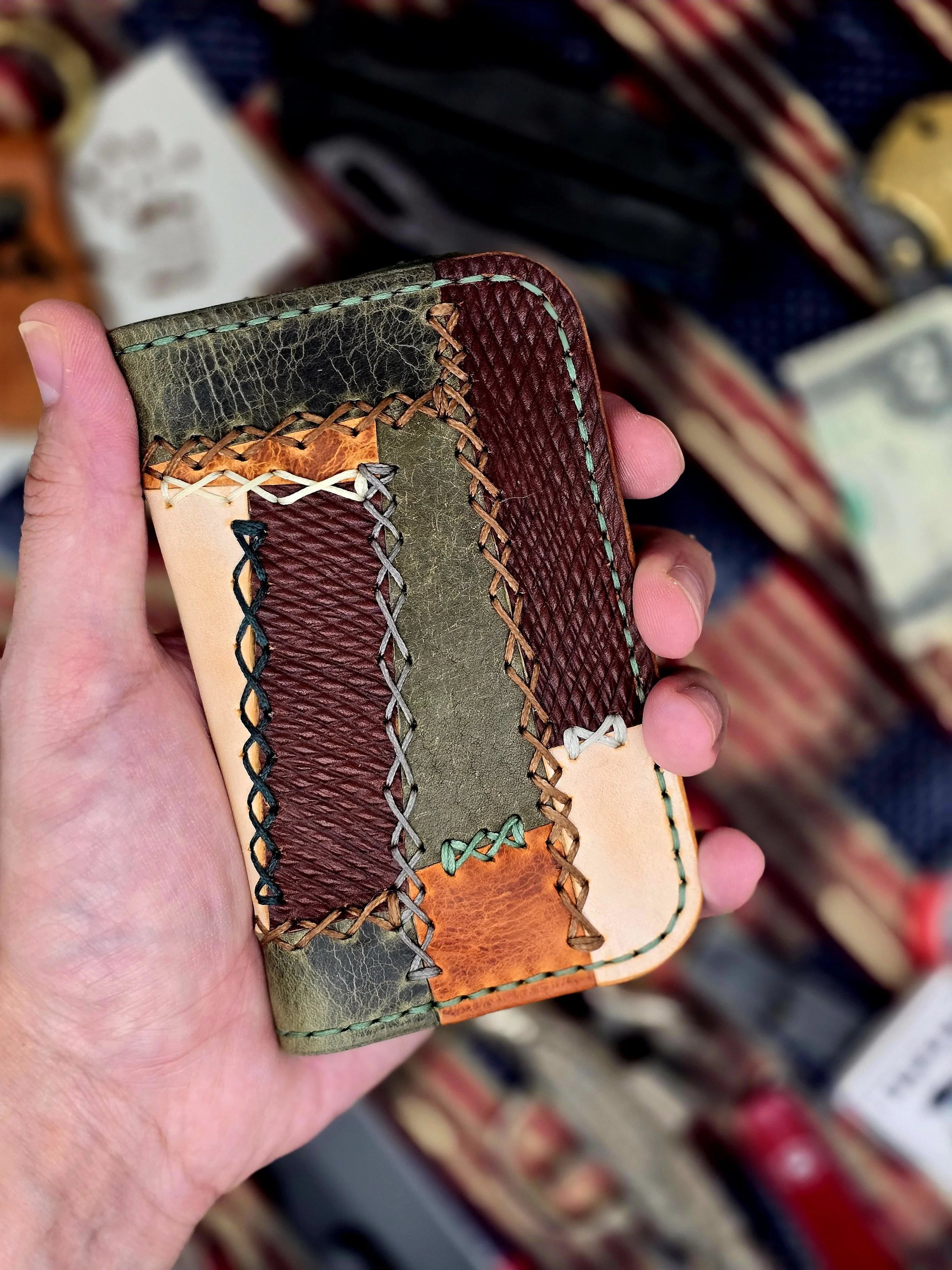 A hand holding a multicolored patchwork leather wallet with various textured and colored sections.