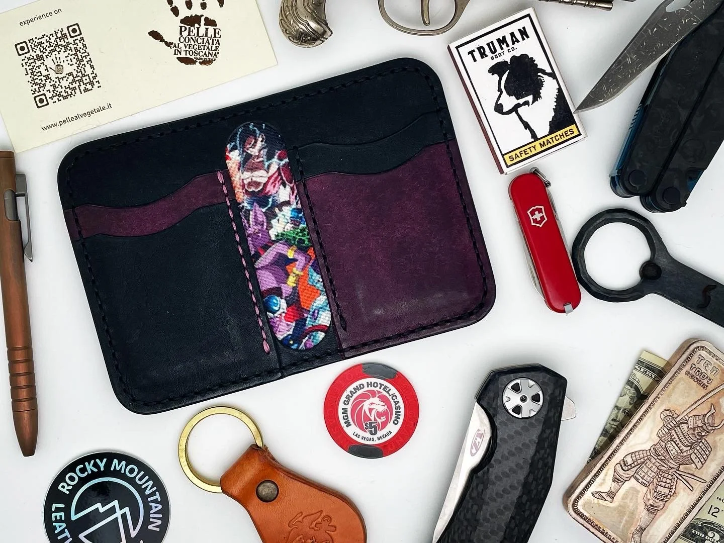Collection of everyday items including a wallet with colorful fabric insert, a Swiss Army knife, a black ring tool, a red multi-tool, a pocket-sized flashlight, a pair of black and gray scissors, a keyring with brown leather key fob, a casino chip, c
