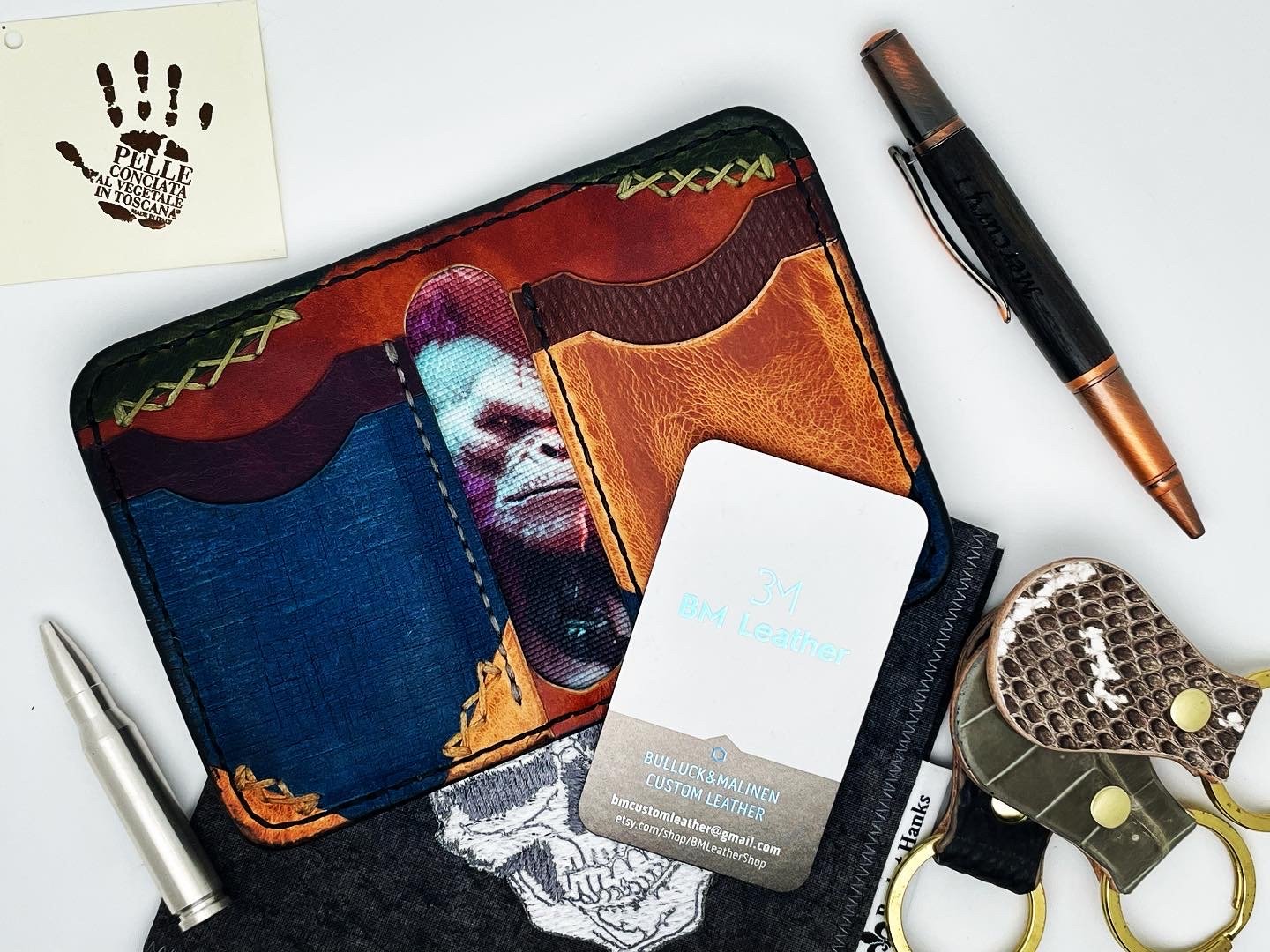 A leather portfolio with a colorful design, featuring a woman's face, alongside pens, a business card, a pair of scissors, and a small post-it note with a handprint and text.