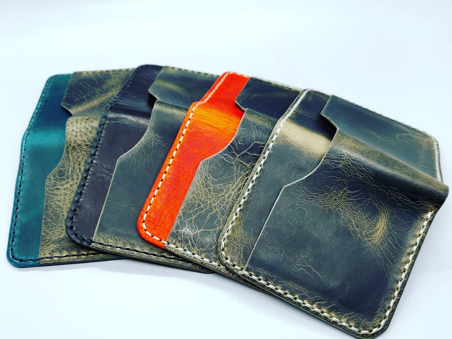 A set of six leather wallets in various colors, including teal, dark blue, orange, green, and black, arranged overlapping on a white surface.