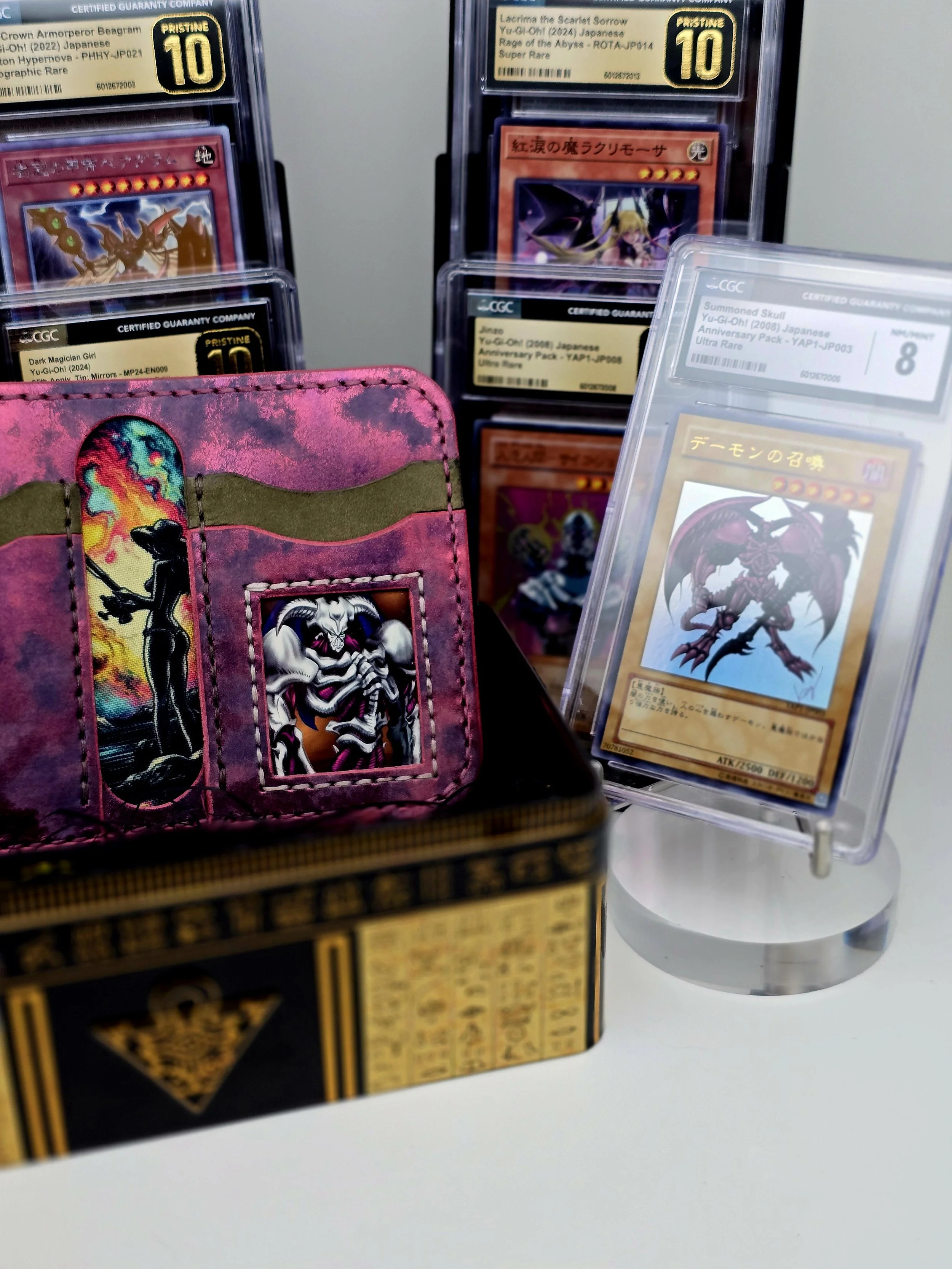 A collection of Yu-Gi-Oh! trading cards in protective sleeves and a colorful card wallet, with some cards featuring anime-style artwork and labels indicating their rarity and grade.