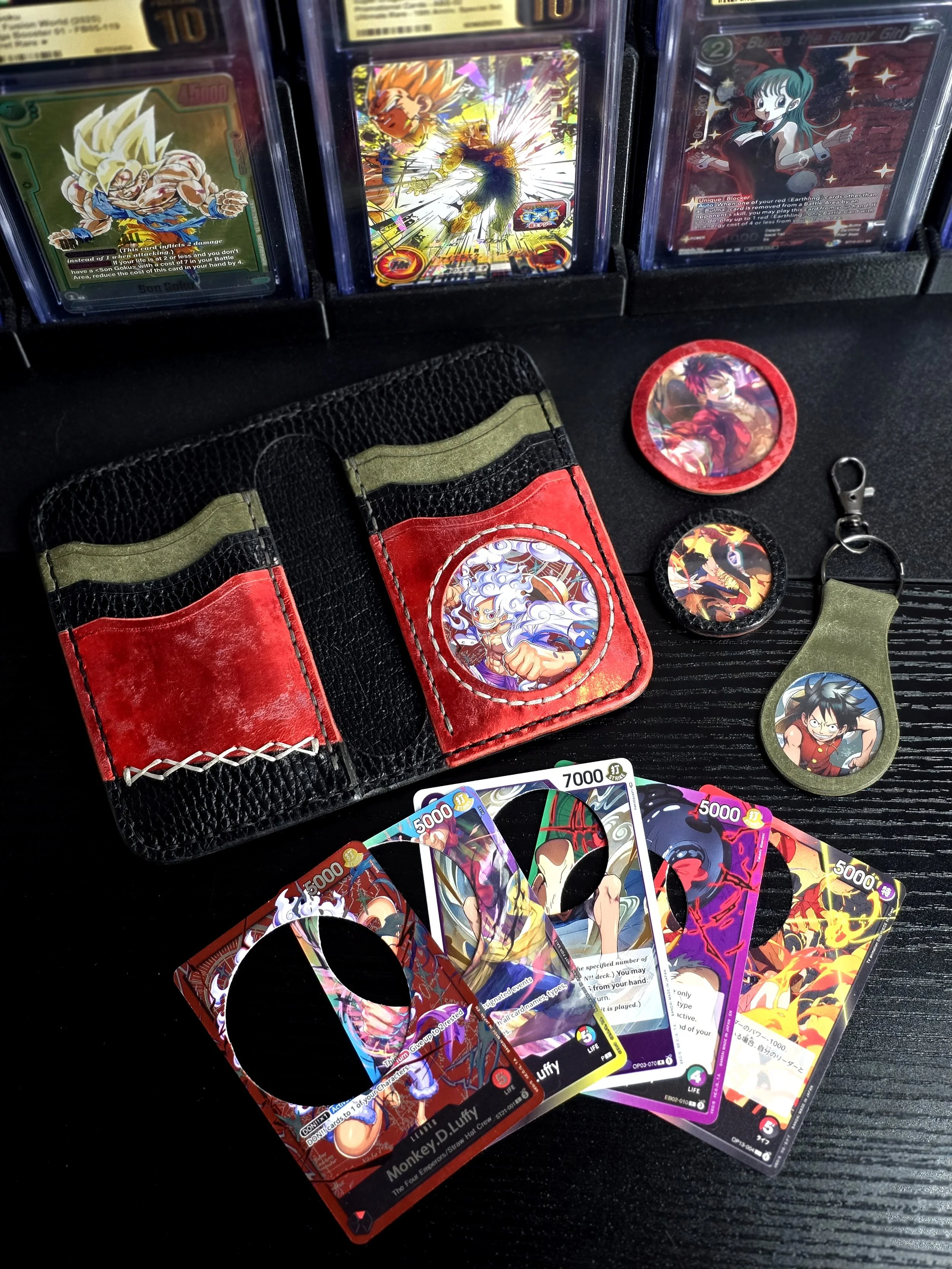Collection of Dragon Ball-themed trading cards, a small wallet with Dragon Ball characters, and various Dragon Ball merchandise, including pins and a keychain, arranged on a black wooden surface.
