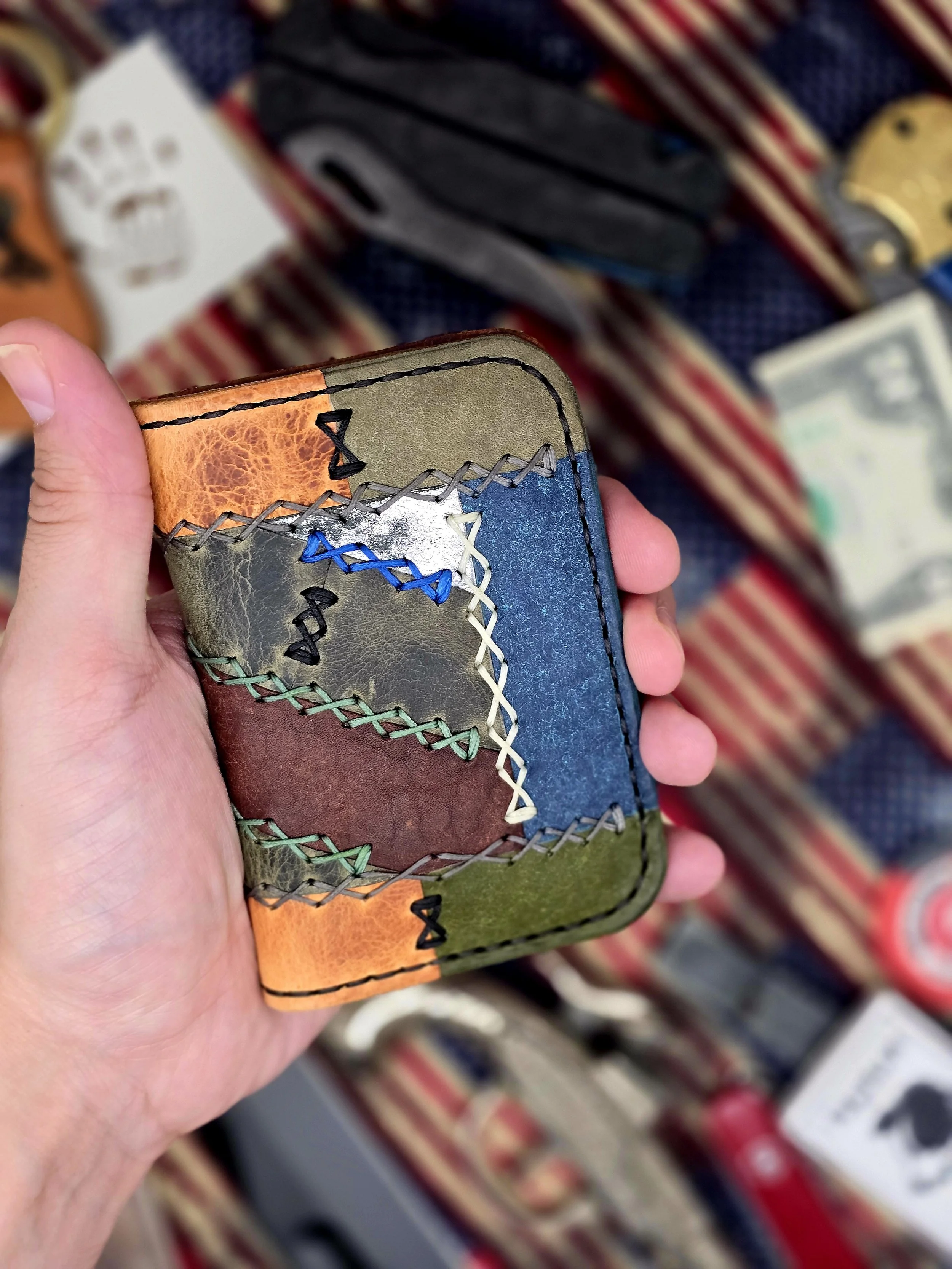Hand holding a colorful, patchwork leather wallet with visible stitching, with a blurred background of similar wallets and cash.