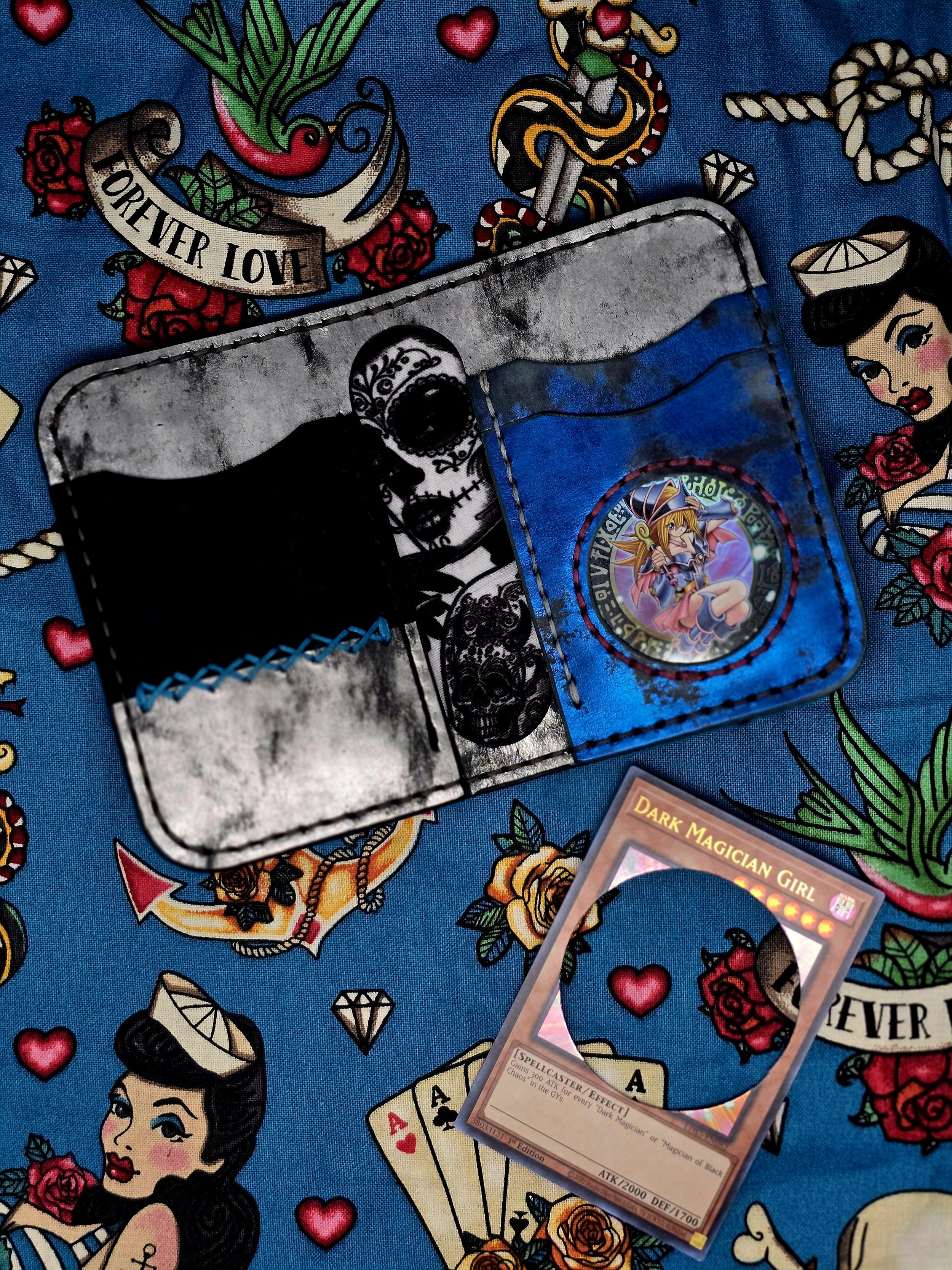 A Yu-Gi-Oh! card titled 'Dark Magician Girl' lying on a colorful, tattoo-inspired cloth with illustrated women, roses, hearts, dice, and banners.