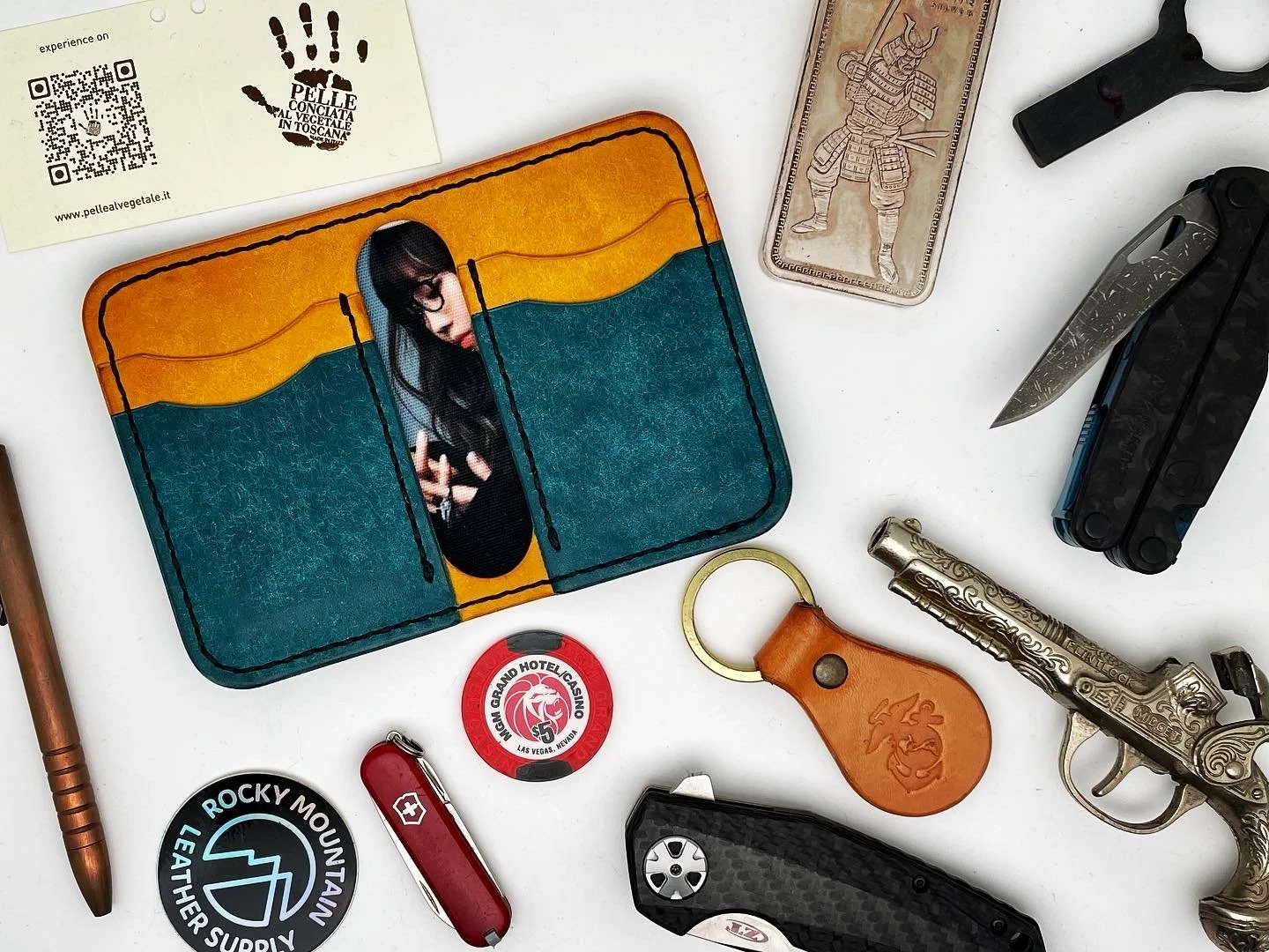 A collection of miscellaneous items on a white surface, including a colorful wallet with an image of a woman on it, a high heel shoe-shaped soap, a folding knife, a fire starter tool, a leather keychain with a lion logo, a small round object with hot