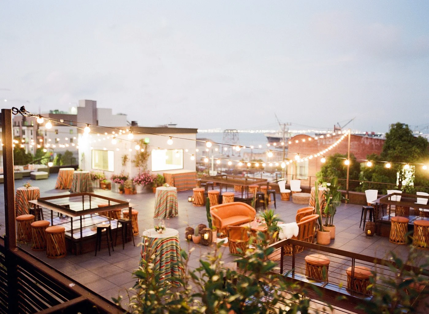 a wedding reception in an open space with tea lights hanging up around it and pops of orange colored furniture and striped tables