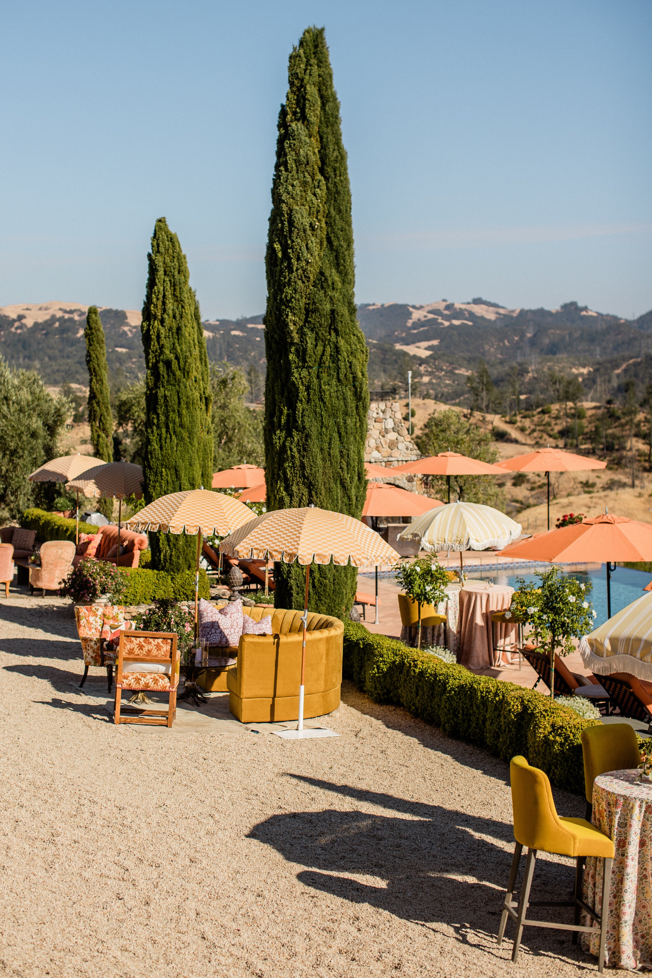 brightly colored orange umbrellas over yellow couches with Cyprus trees around them and a pool with mountains in the background a sonoma wedding venue