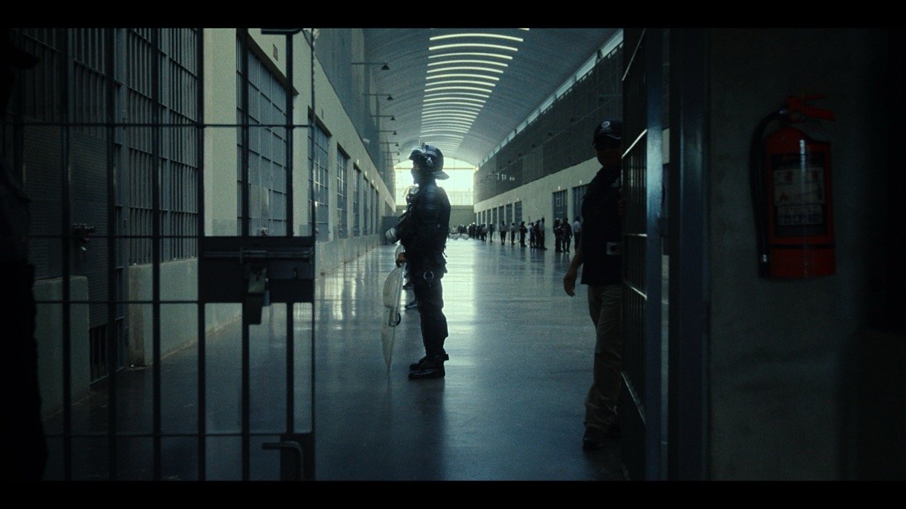 Security personnel standing guard inside a modern building corridor with a high, curved ceiling, and a large group of people in the distance.