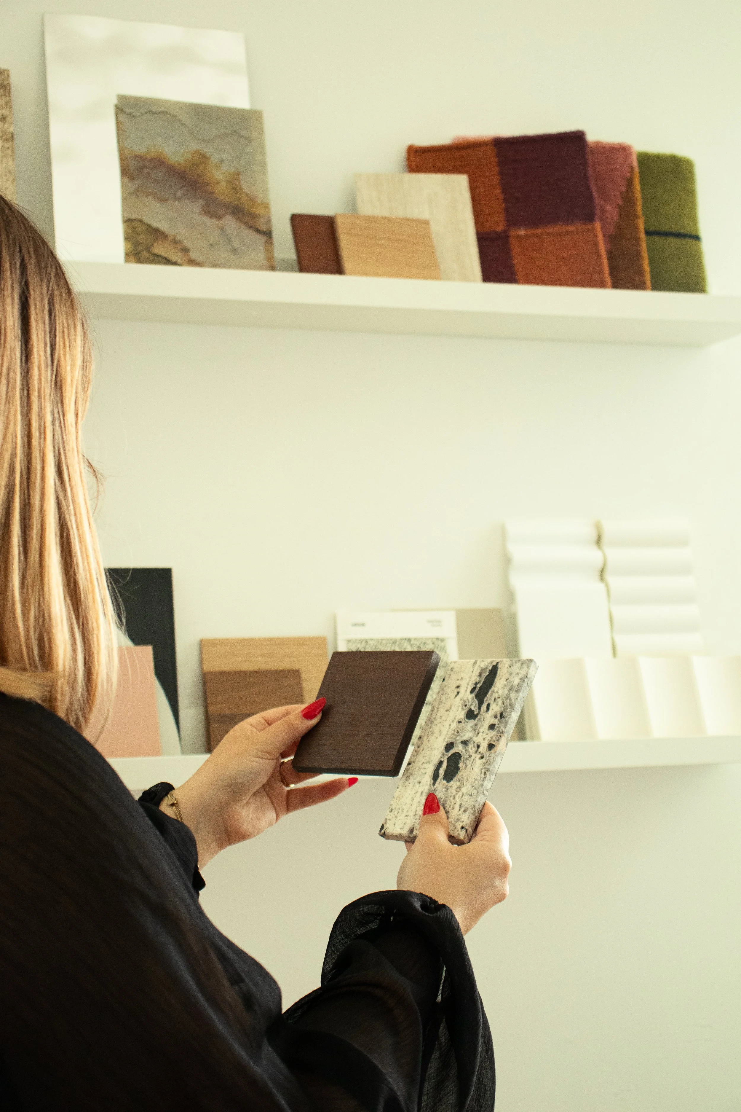 Une femme tient deux échantillons de matériaux de décoration, l'un en bois foncé et l'autre en marbre blanc avec des motifs noirs.